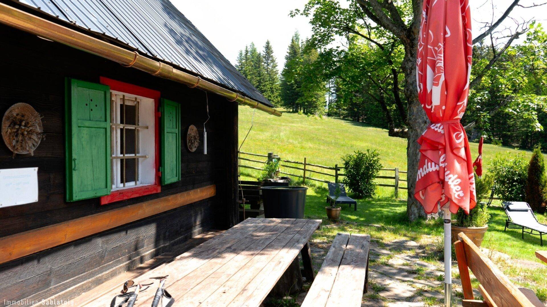 Rustikales Holzhaus mit grünen Fensterläden und einem einladenden Picknicktisch im Gartenbereich.