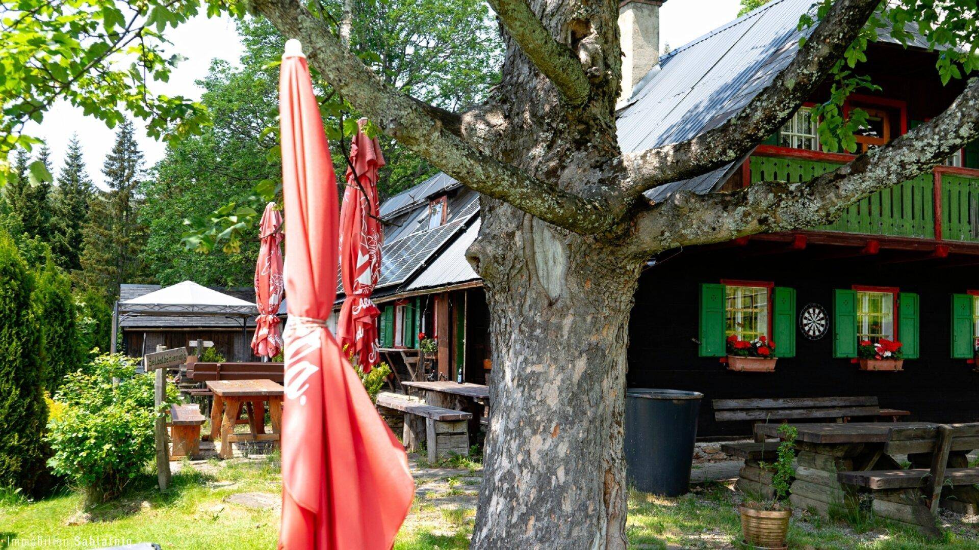 Rustikaler Außenbereich mit Holztischen und Sonnenschirmen vor einem traditionellen Holzhaus.