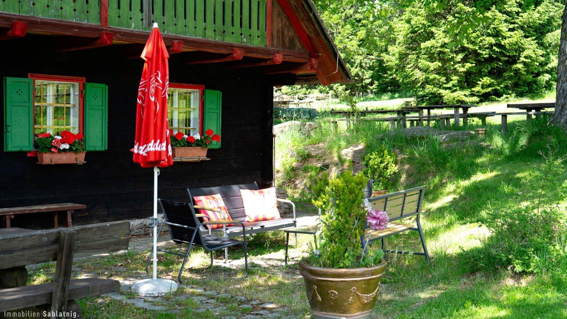 Detailansicht des Holzhauses mit grünen Fensterläden, Blumenkästen und gemütlicher Sitzgelegenheit im Freien.