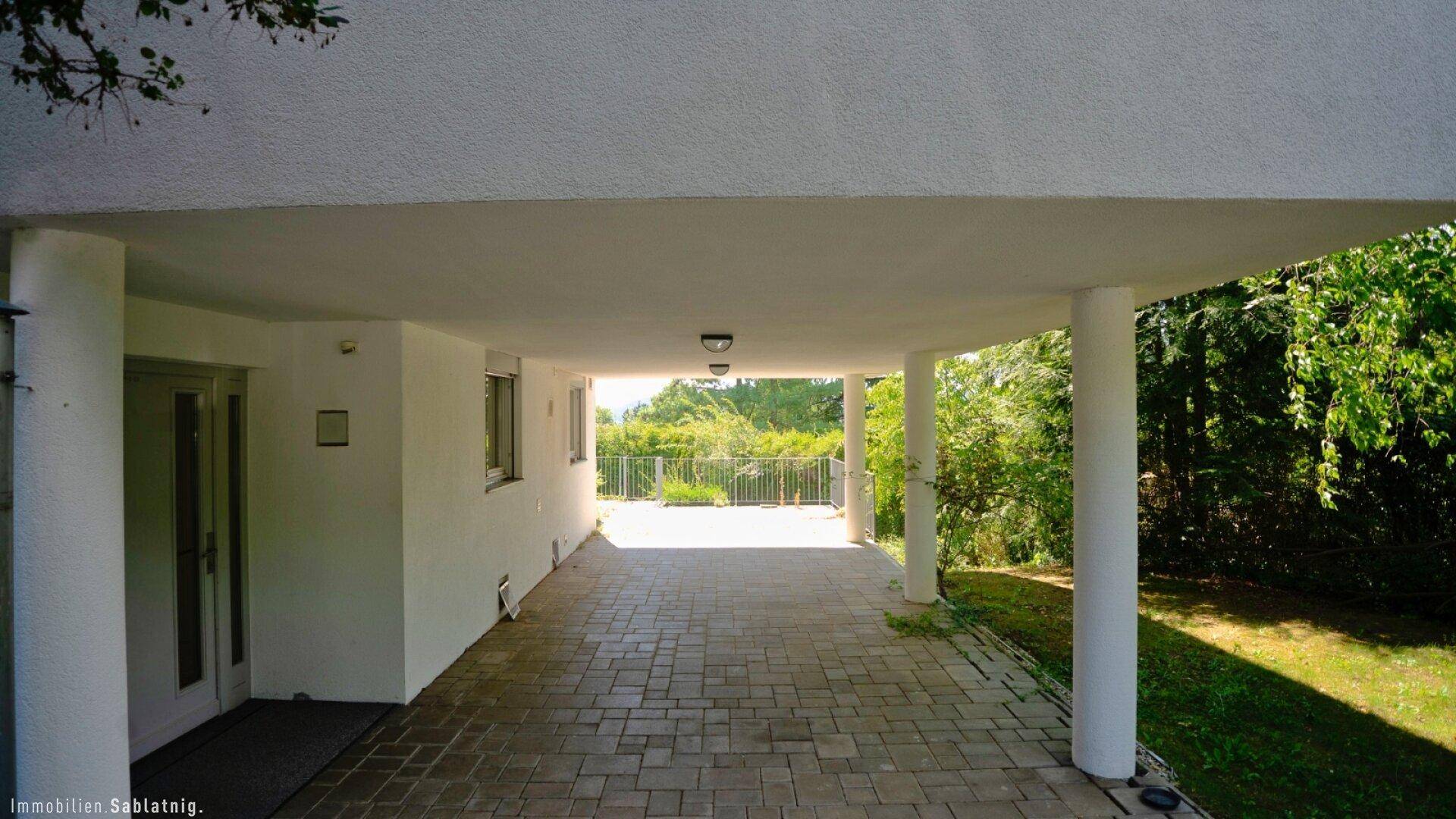 Überdachter Carport-Bereich mit gepflastertem Boden und Säulen, bietet Schutz für Fahrzeuge.