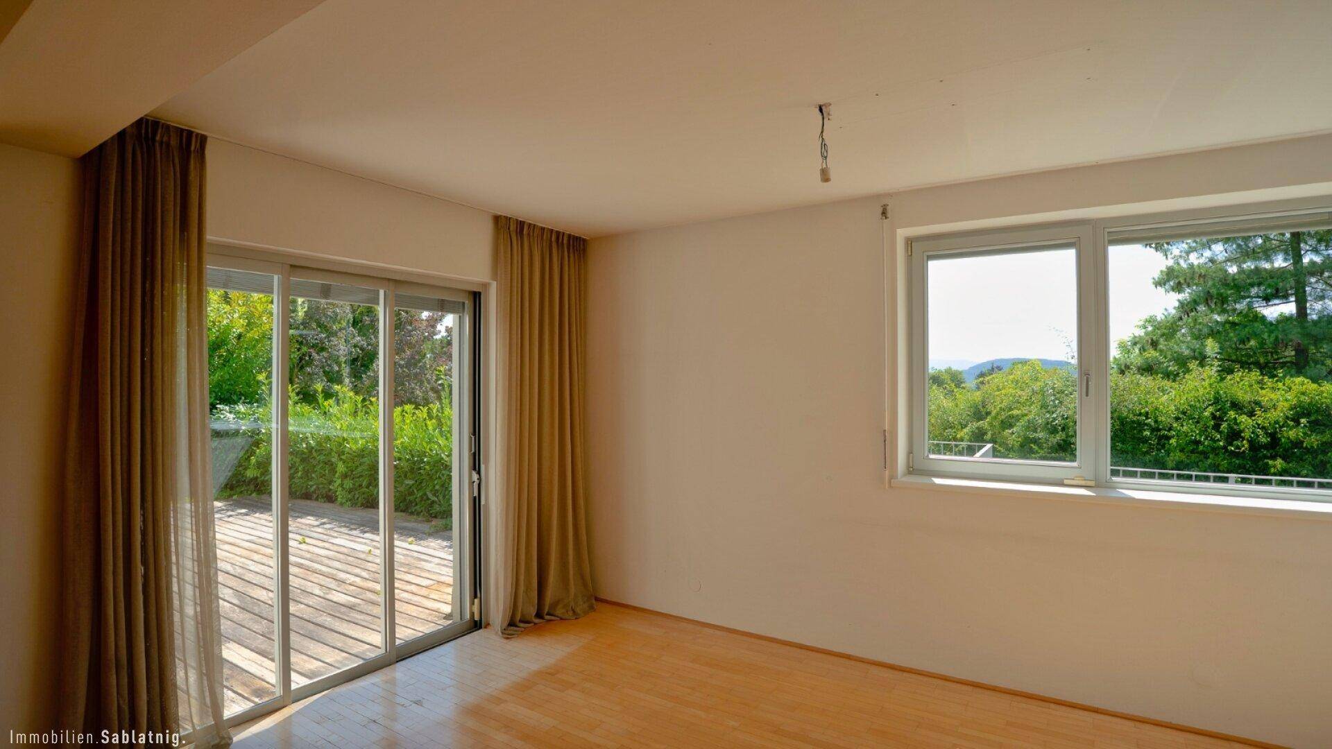 Helles Zimmer mit Holzfußboden, großen Fenstern und direktem Zugang zu einem Außenbereich.