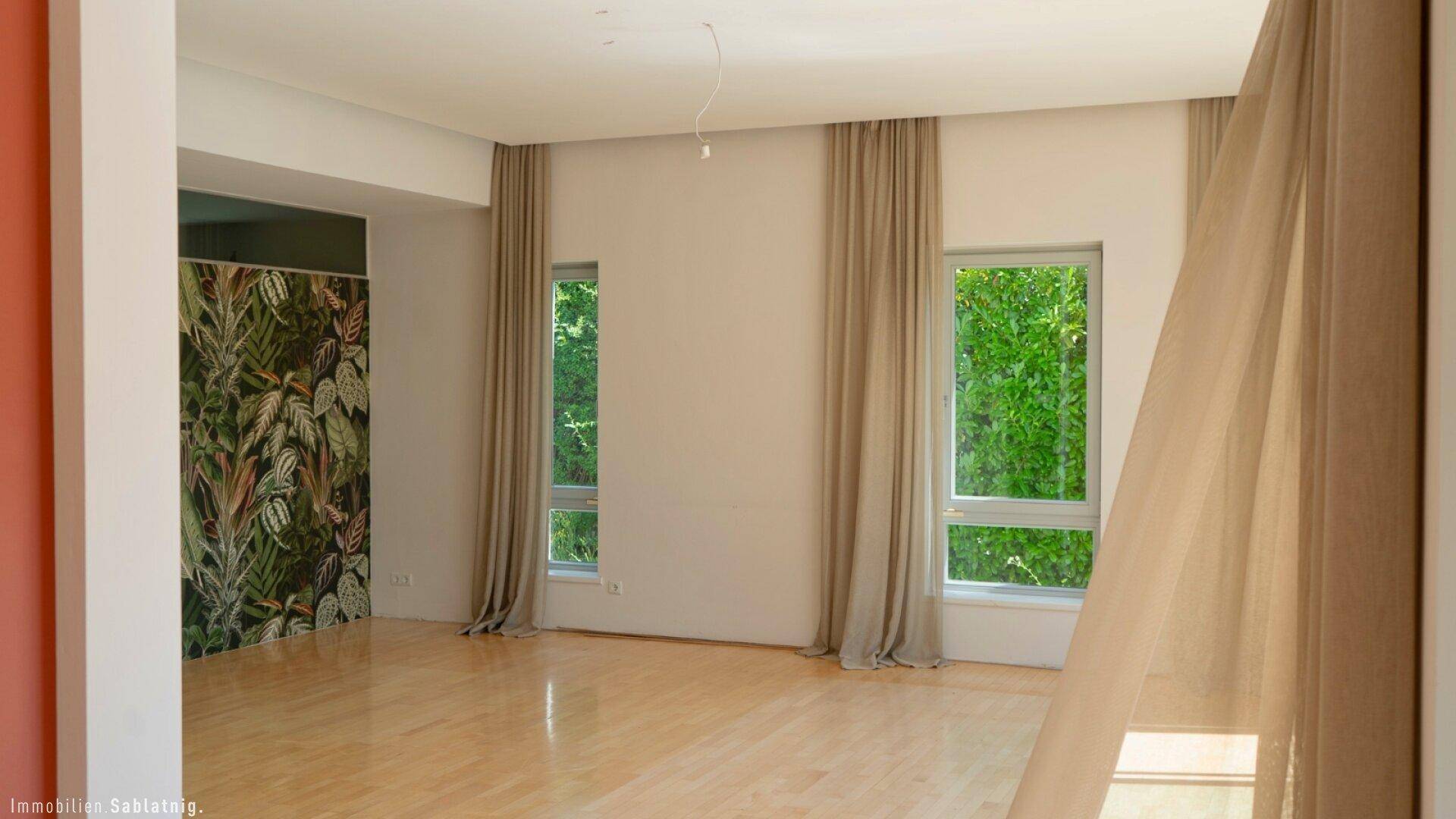Helles Wohnzimmer mit dekorativer Tapetenwand, hohen Fenstern und Vorhängen.