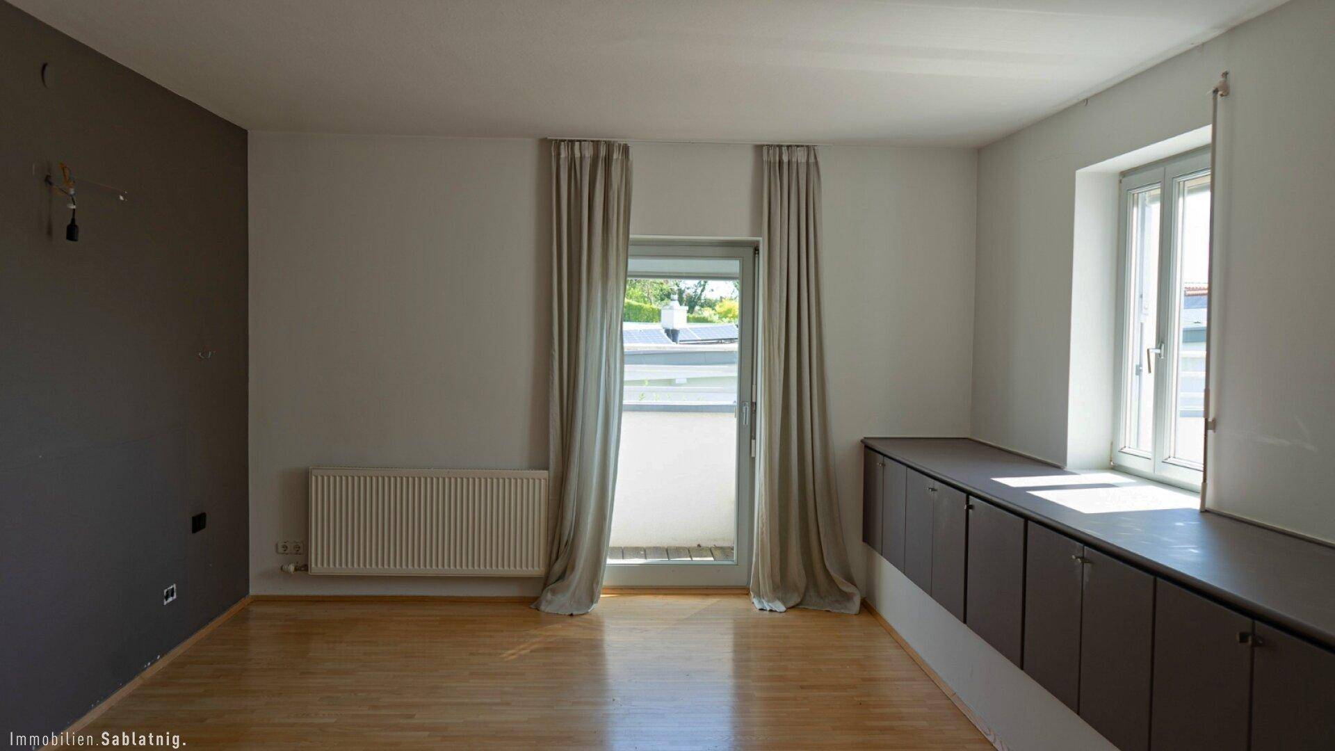 Helles Zimmer mit Heizkörper, Zugang zu einem französischen Balkon und eingebauten Schränken.