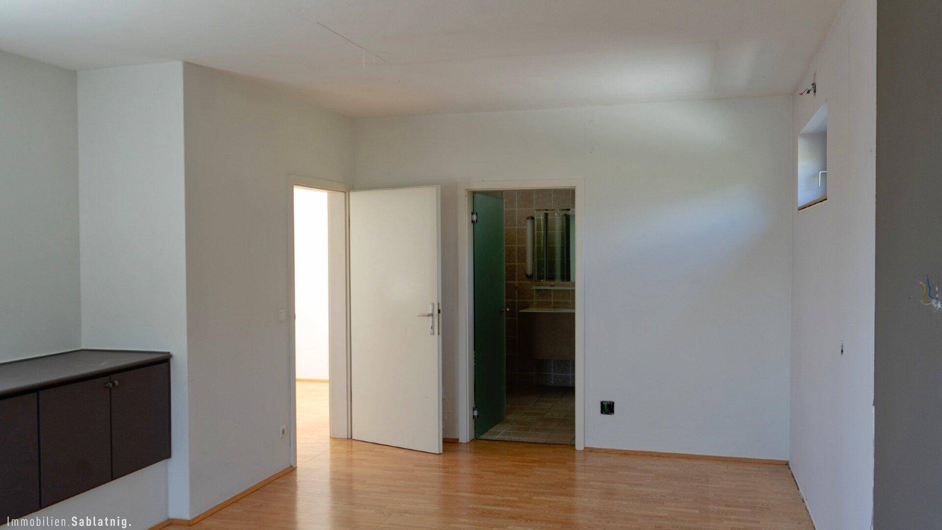 Geräumiges Zimmer mit hellem Holzfußboden und zwei Türen, eine davon führt ins Badezimmer.