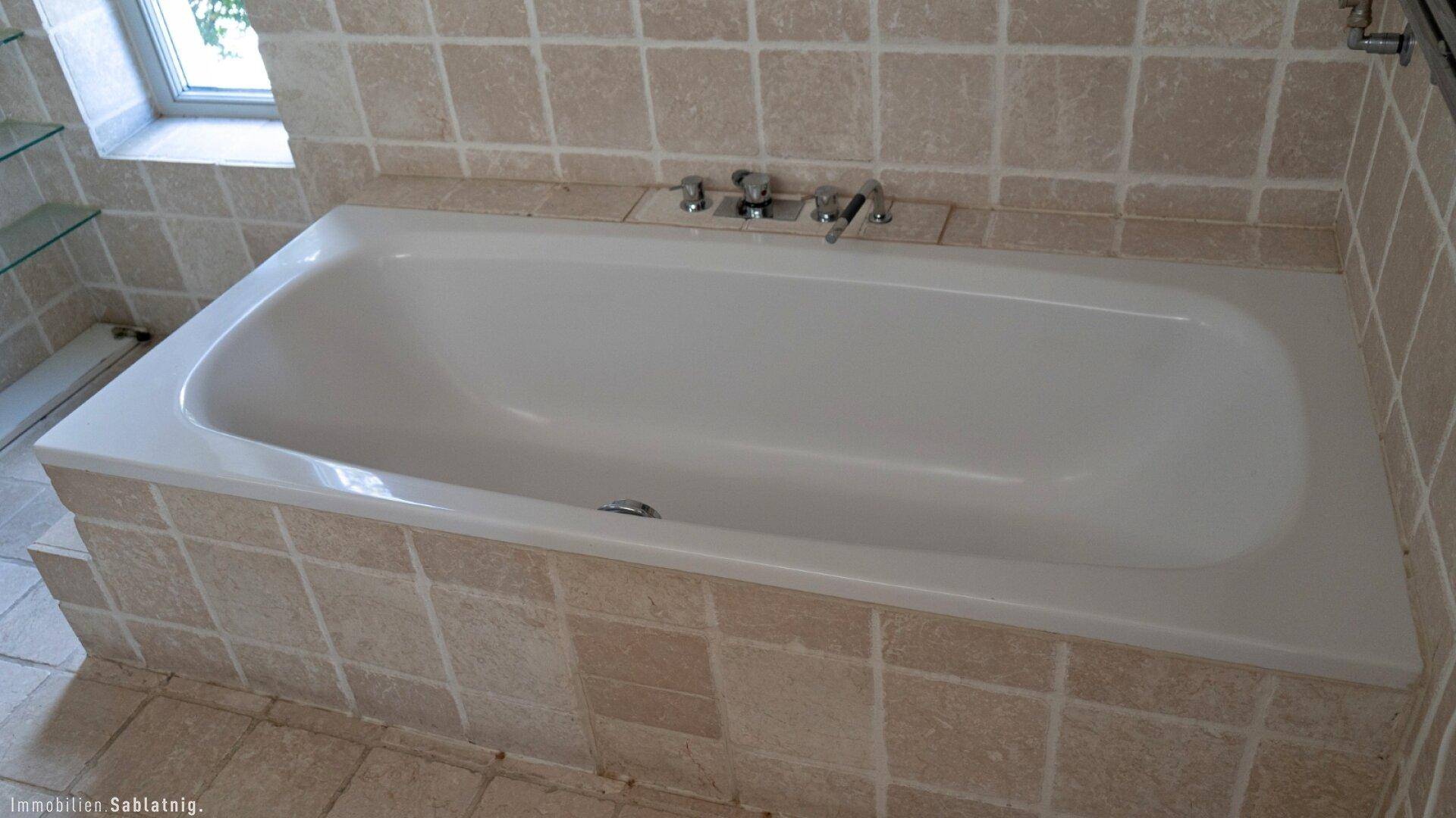 Badezimmer mit eingebauter Badewanne und beigefarbenen Fliesen an Wänden und Boden.