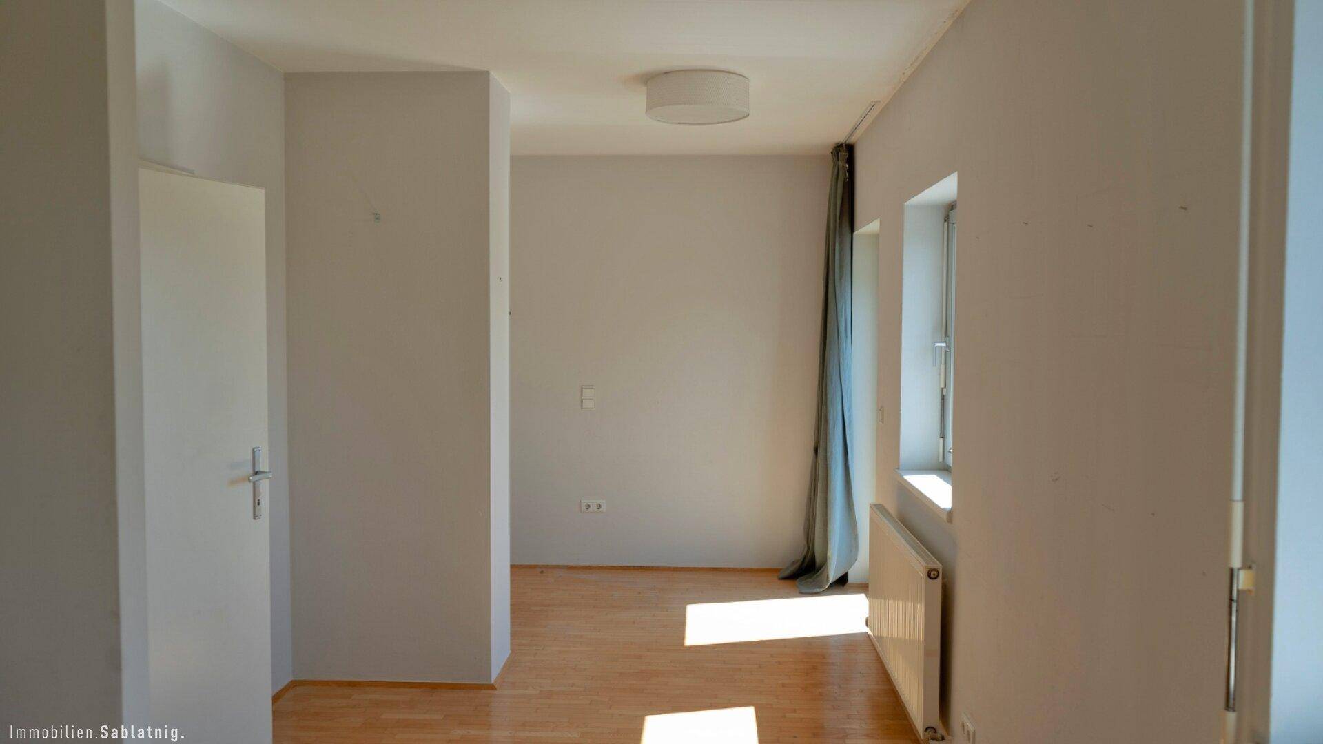 Helles Zimmer mit Holzfußboden, Heizkörper und Fenster, bietet vielseitige Nutzungsmöglichkeiten.