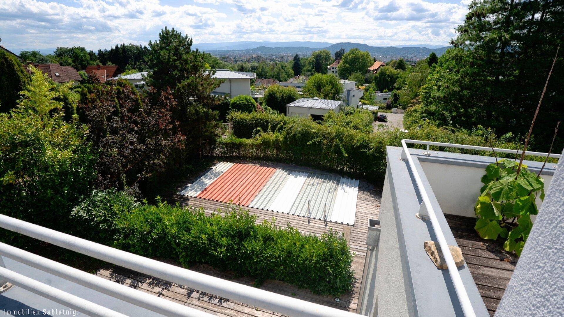 Große Terrasse mit Blick auf den Poolbereich, umgeben von viel Grün und einer weiten Aussicht auf die Stadt und Berge.