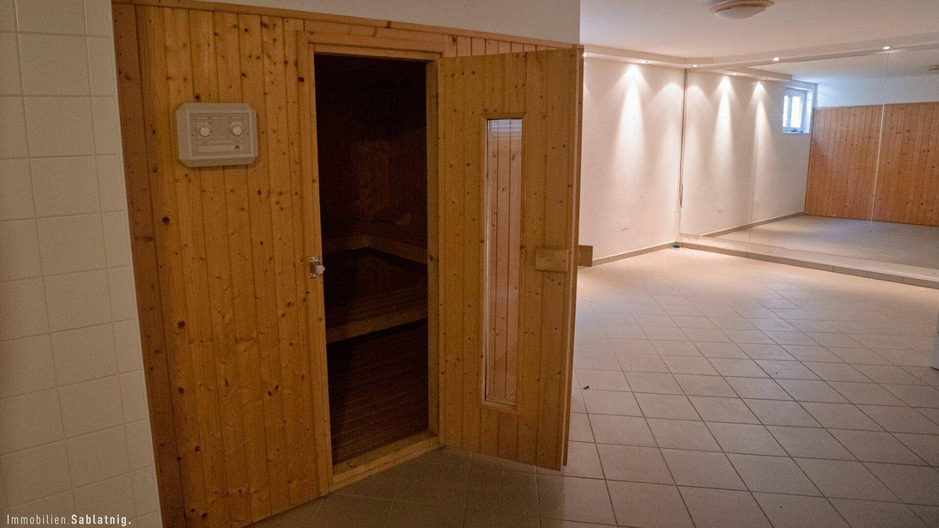 Geräumiger Wellnessbereich mit einer Holzkabine für die Sauna und hellem Fliesenboden.