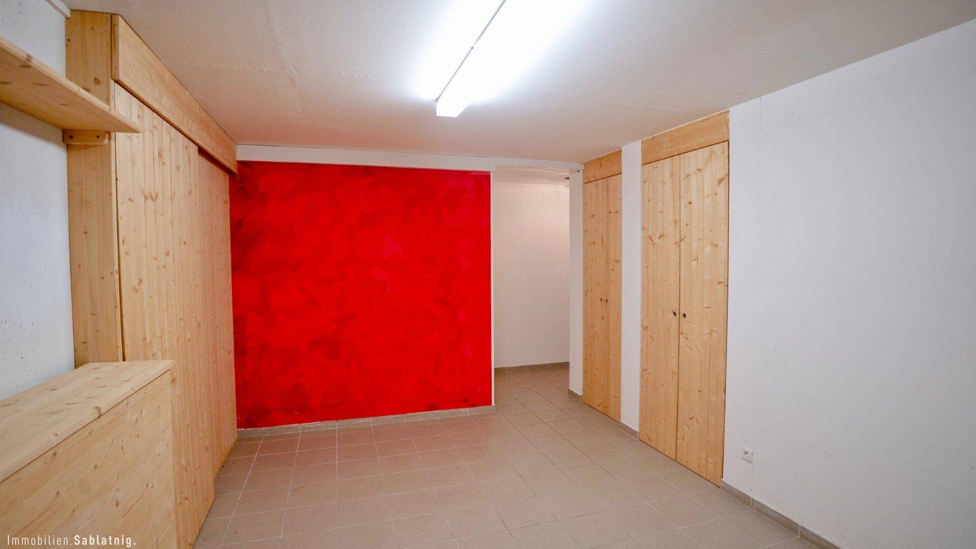 Funktionaler Raum mit Fliesenboden, einer roten Akzentwand und Holzverkleidungen, ideal als Abstell- oder Hobbyraum.