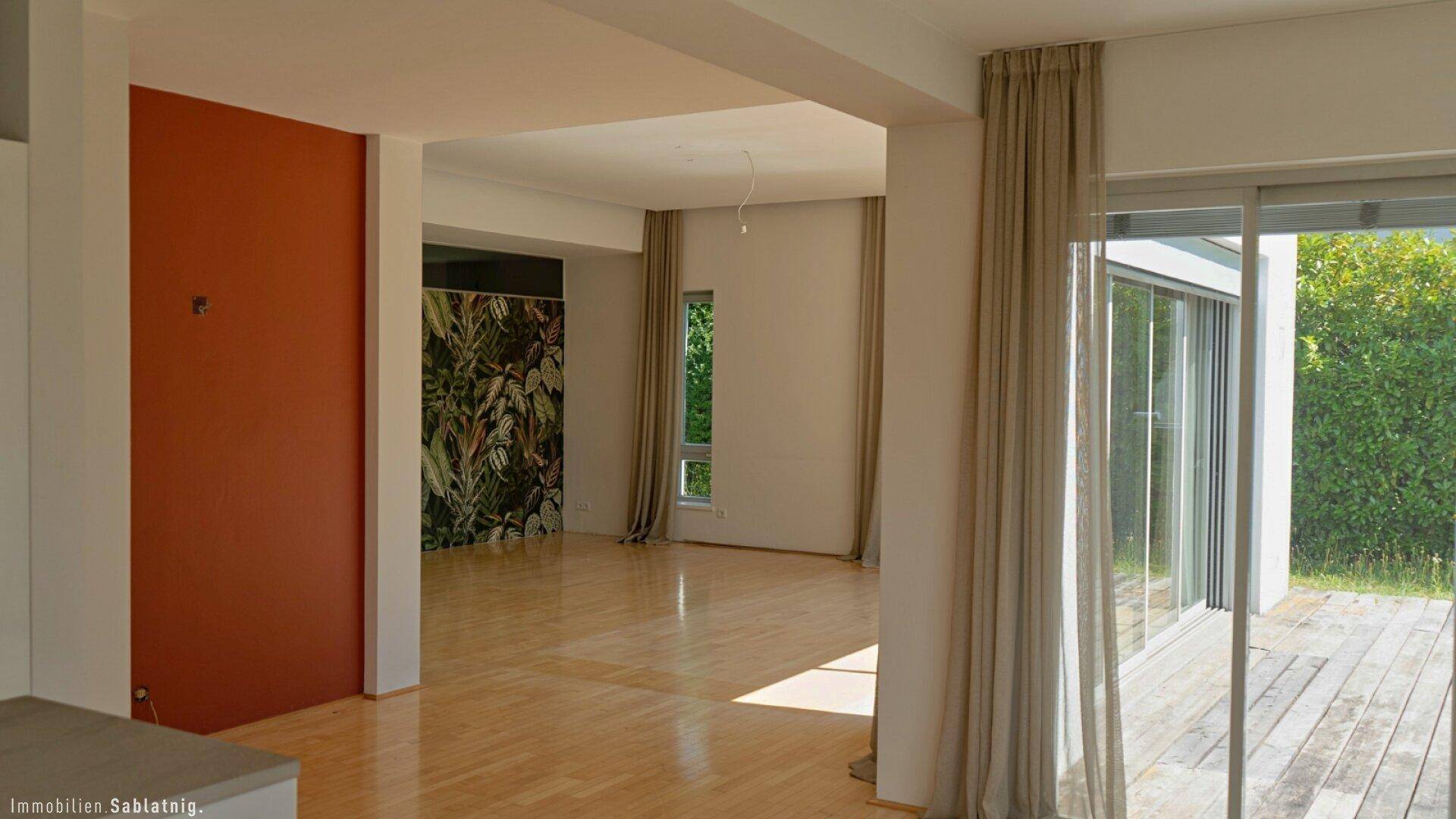 Offener Wohnbereich mit hellem Holzfußboden, dekorativer Wand und Zugang zur Terrasse.