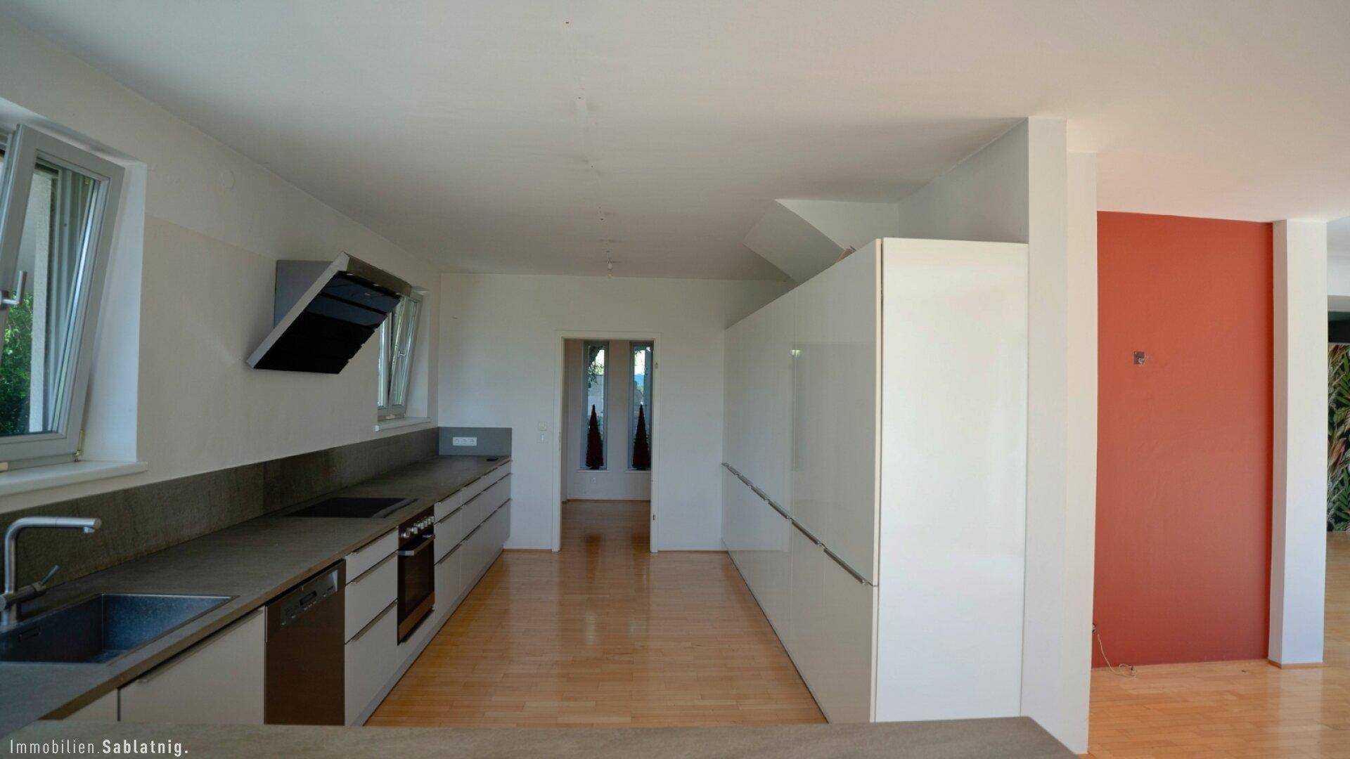 Blick vom Wohnbereich in die moderne Küche mit weißen Hochglanzschränken und integrierten Geräten.