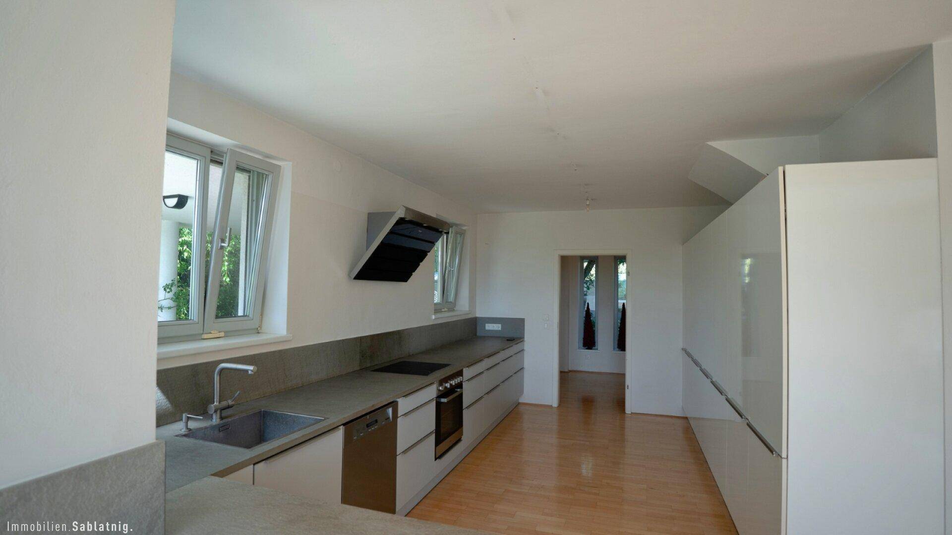 Moderne Küche mit grauen Unterschränken, integrierten Geräten und hellem Holzfußboden.