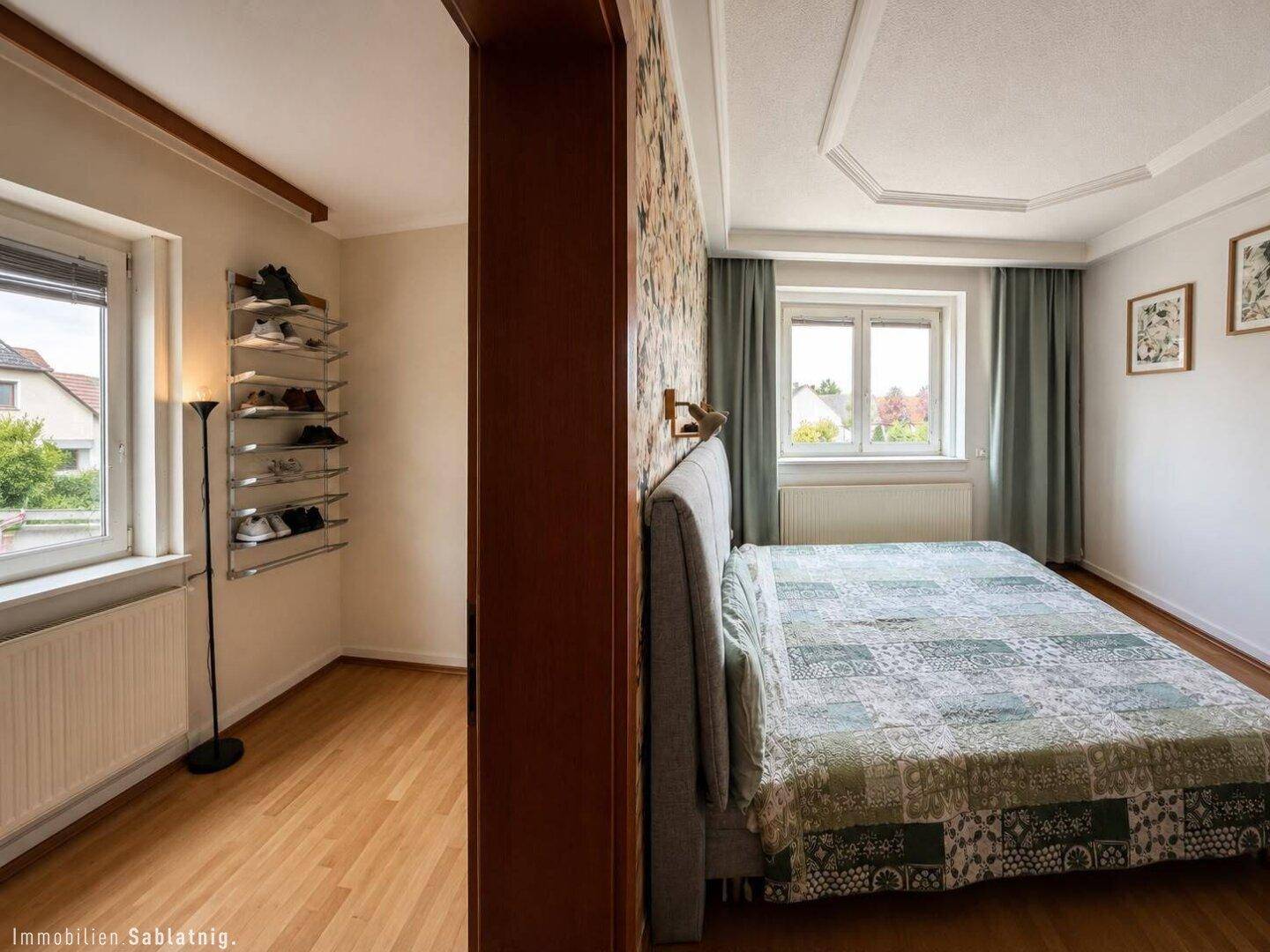 Schlafzimmer mit floraler Akzentwand, Holzboden und Blick auf die Umgebung.