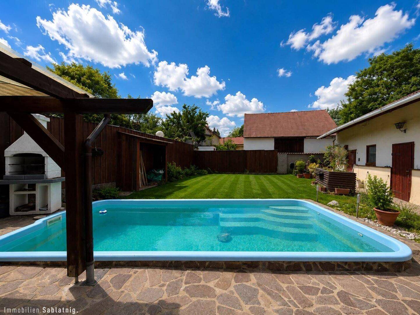 Gepflegter Gartenbereich mit Rasenfläche, Swimmingpool und Grillstelle.