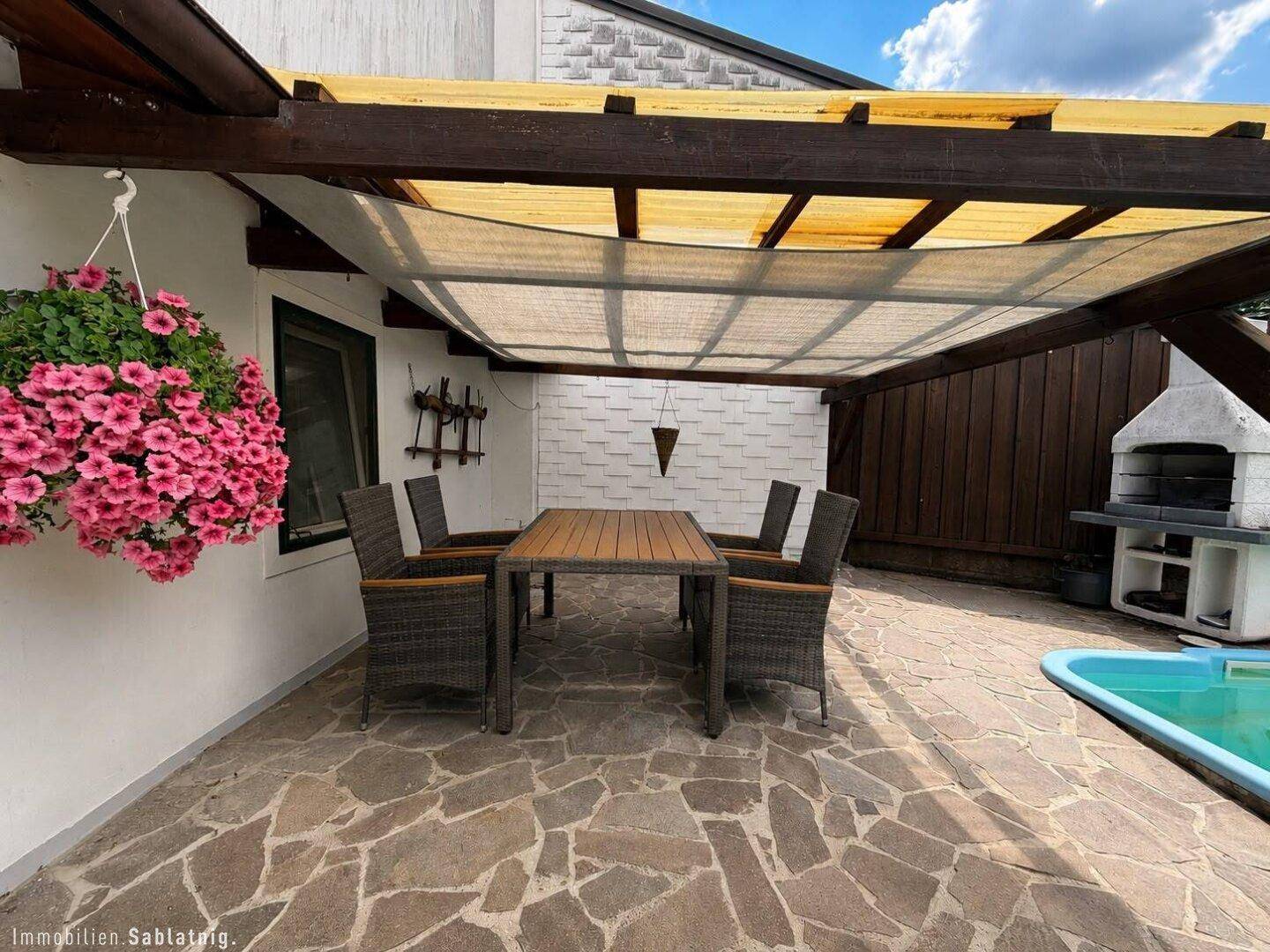 Überdachte Terrasse mit Sitzgelegenheiten, Grillplatz und Zugang zum Poolbereich.