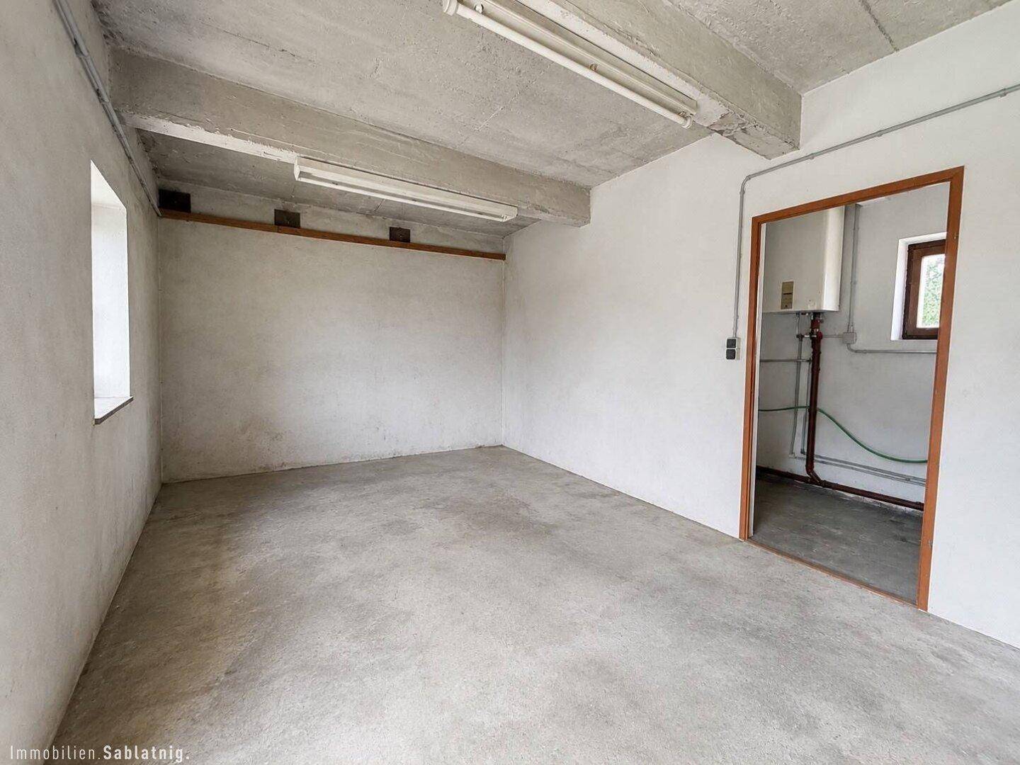 Geräumiger Kellerraum mit Betonboden und Zugang zu einem Technikraum.