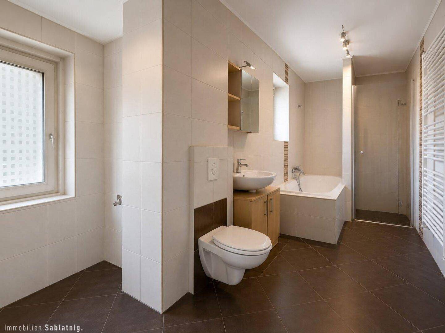 Modernes Badezimmer mit dunklen Bodenfliesen, Badewanne, Dusche und Fenster.
