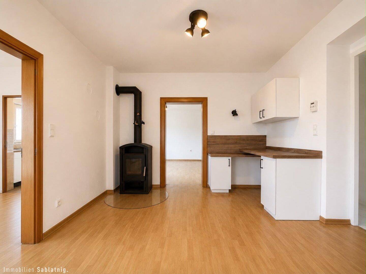 Heller Wohnbereich mit Holzboden, einem modernen Holzofen und kleiner Küchenzeile.