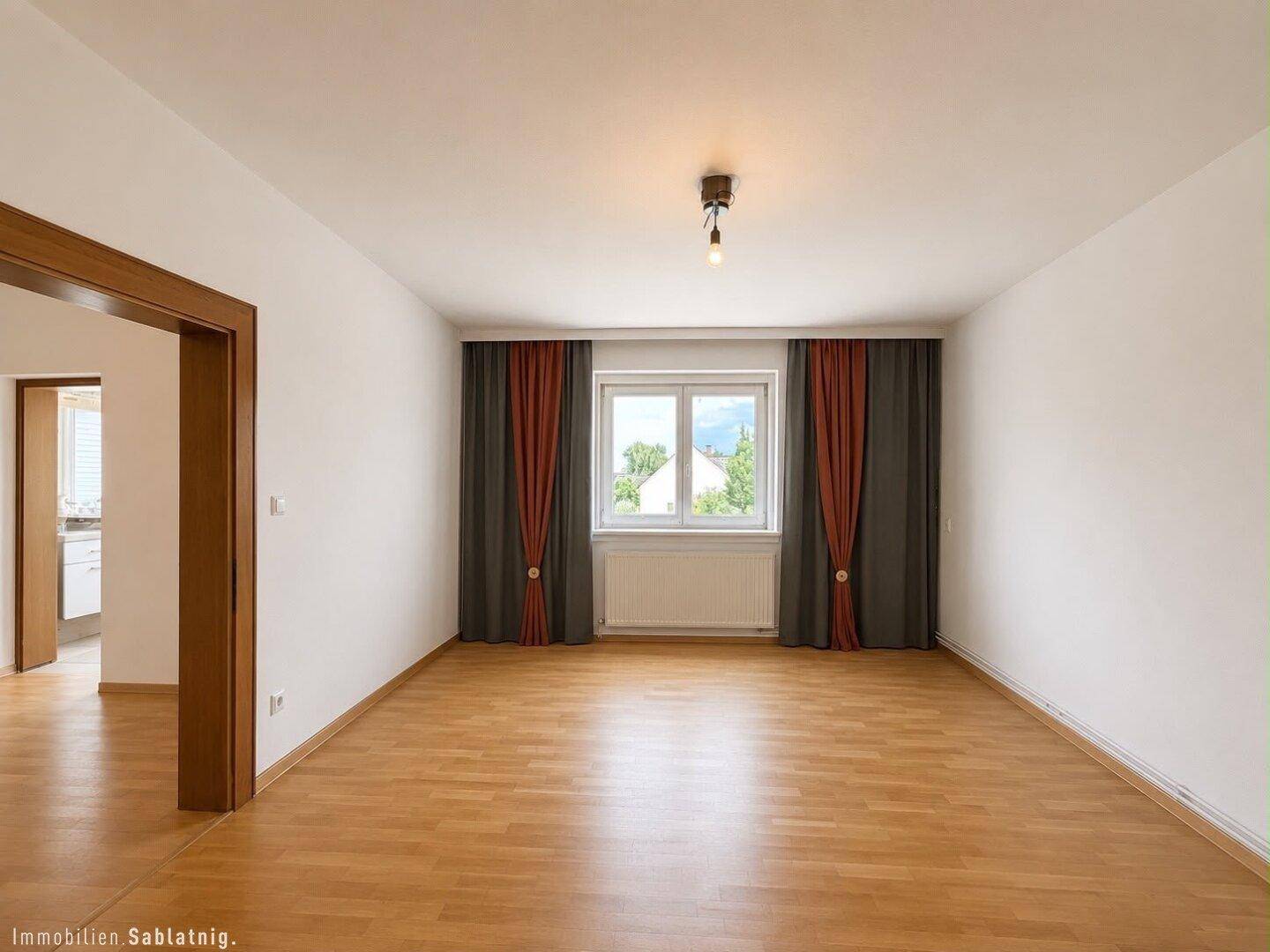 Geräumiges Wohnzimmer mit hellem Holzboden und großen Fenstern, bereit zur Einrichtung.