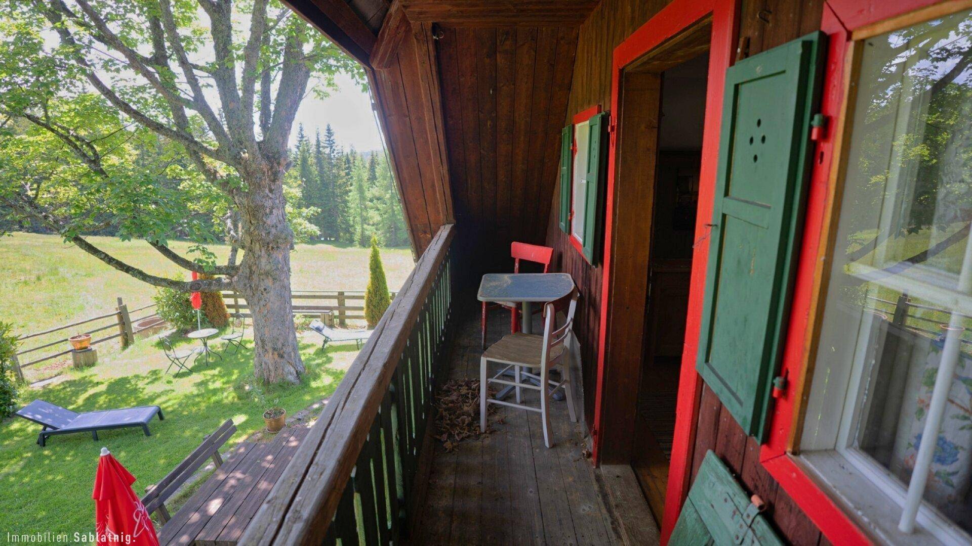 Sonniger Holzbalkon mit Sitzgelegenheiten und weitem Blick über die grüne Landschaft.