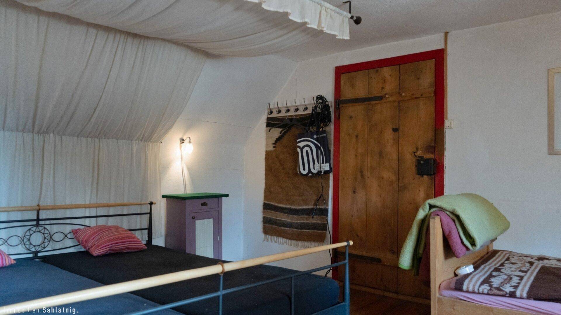 Schlafzimmer mit Metallbettgestell, Holzboden und dekorativem Wandteppich in rustikalem Stil.