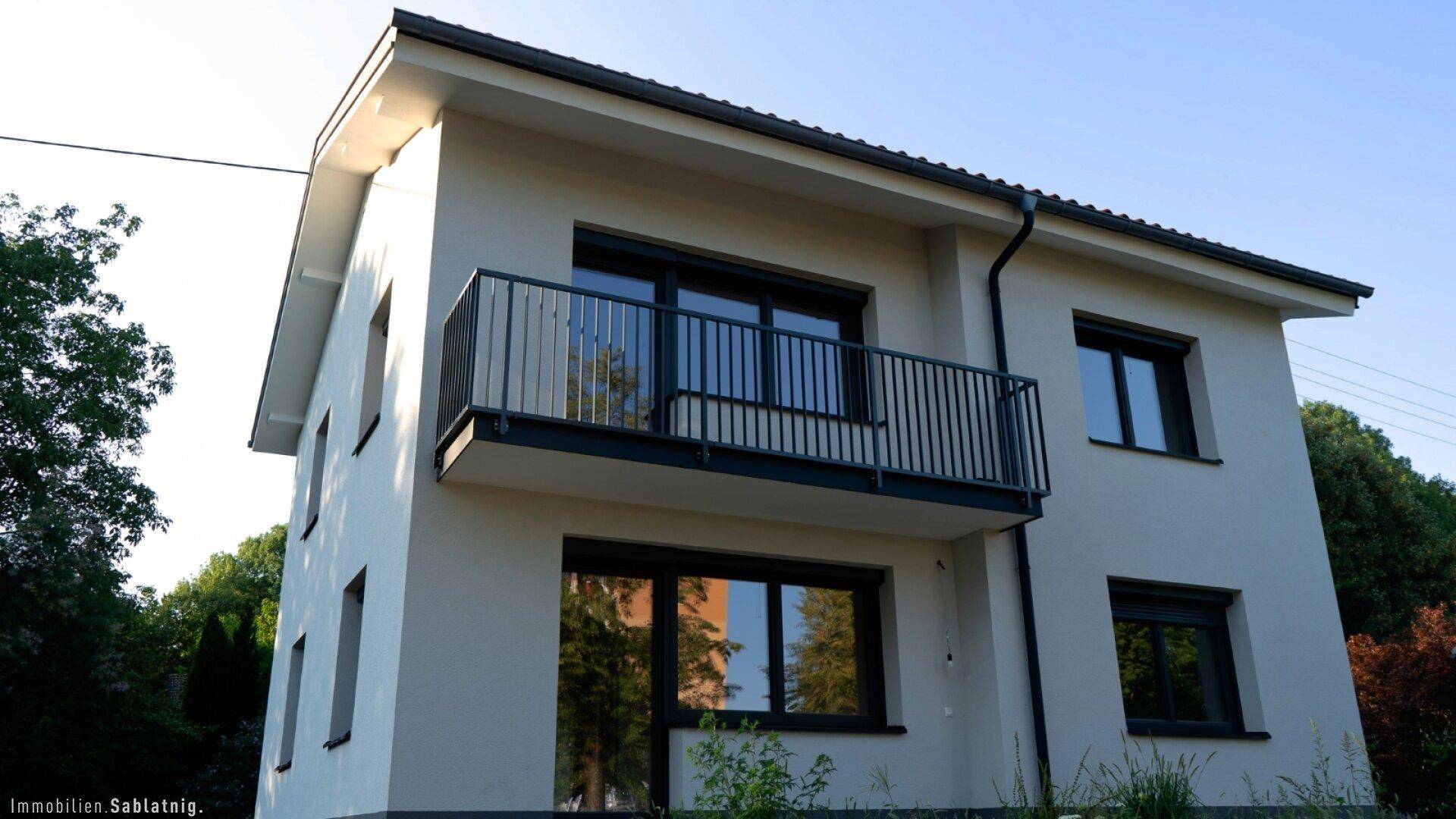 Ansicht des modernen Einfamilienhauses mit Balkon und dunklen Fensterrahmen.