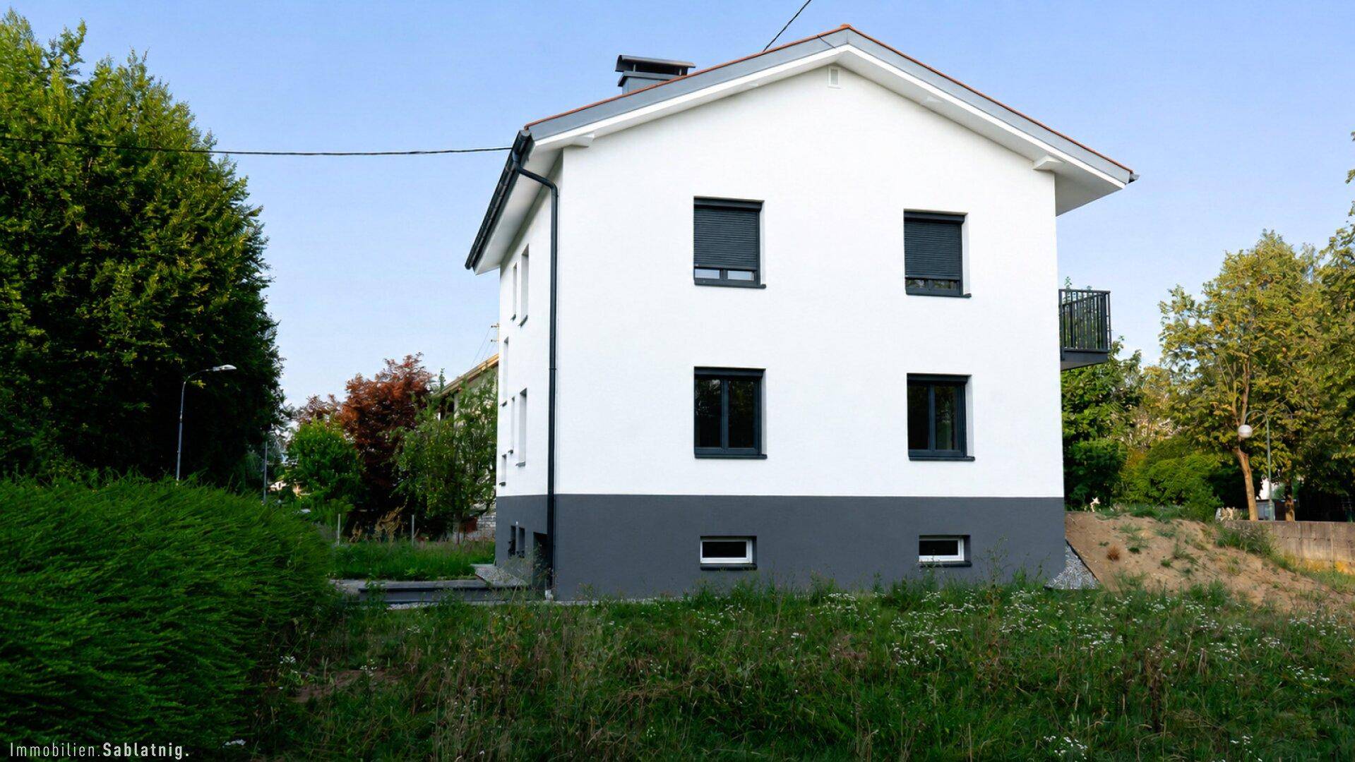 Seitenansicht des modernen Einfamilienhauses mit weißer Fassade und grüner Umgebung.
