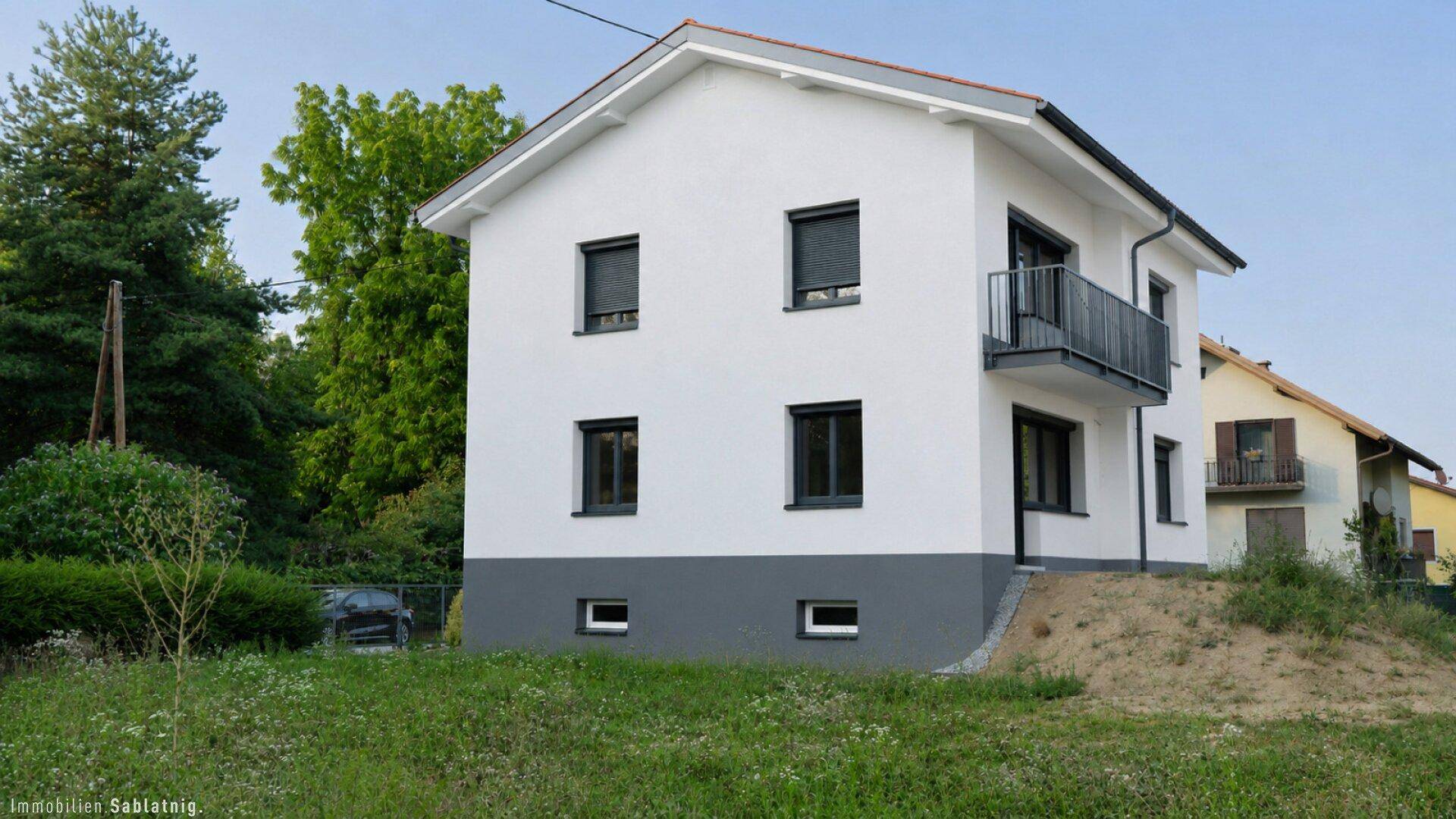 Rückansicht des Hauses mit weißer Fassade, Rollläden und einem kleinen Balkon.