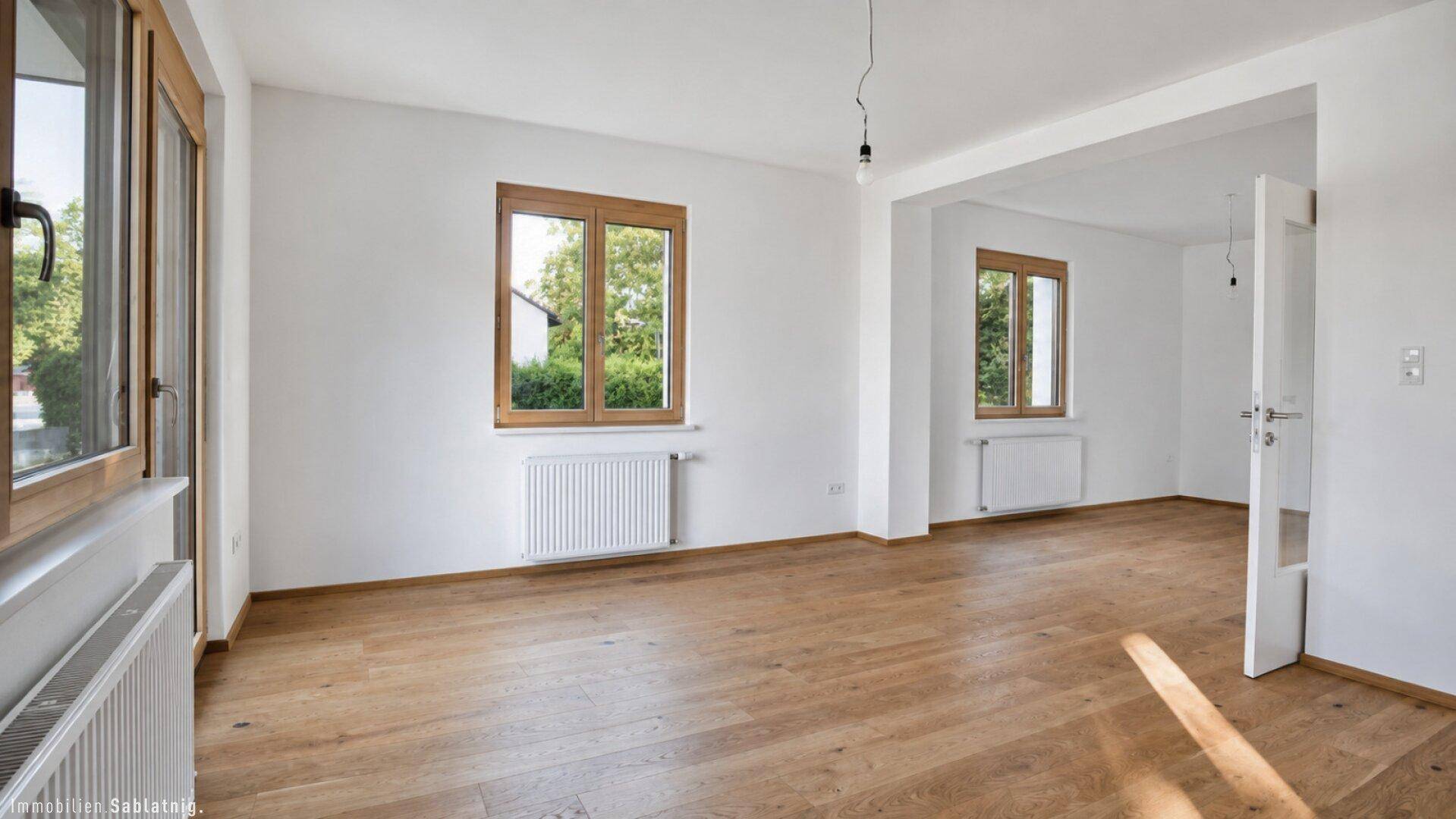 Helles, leeres Wohnzimmer mit Eichenparkettboden und großen Holzfenstern.