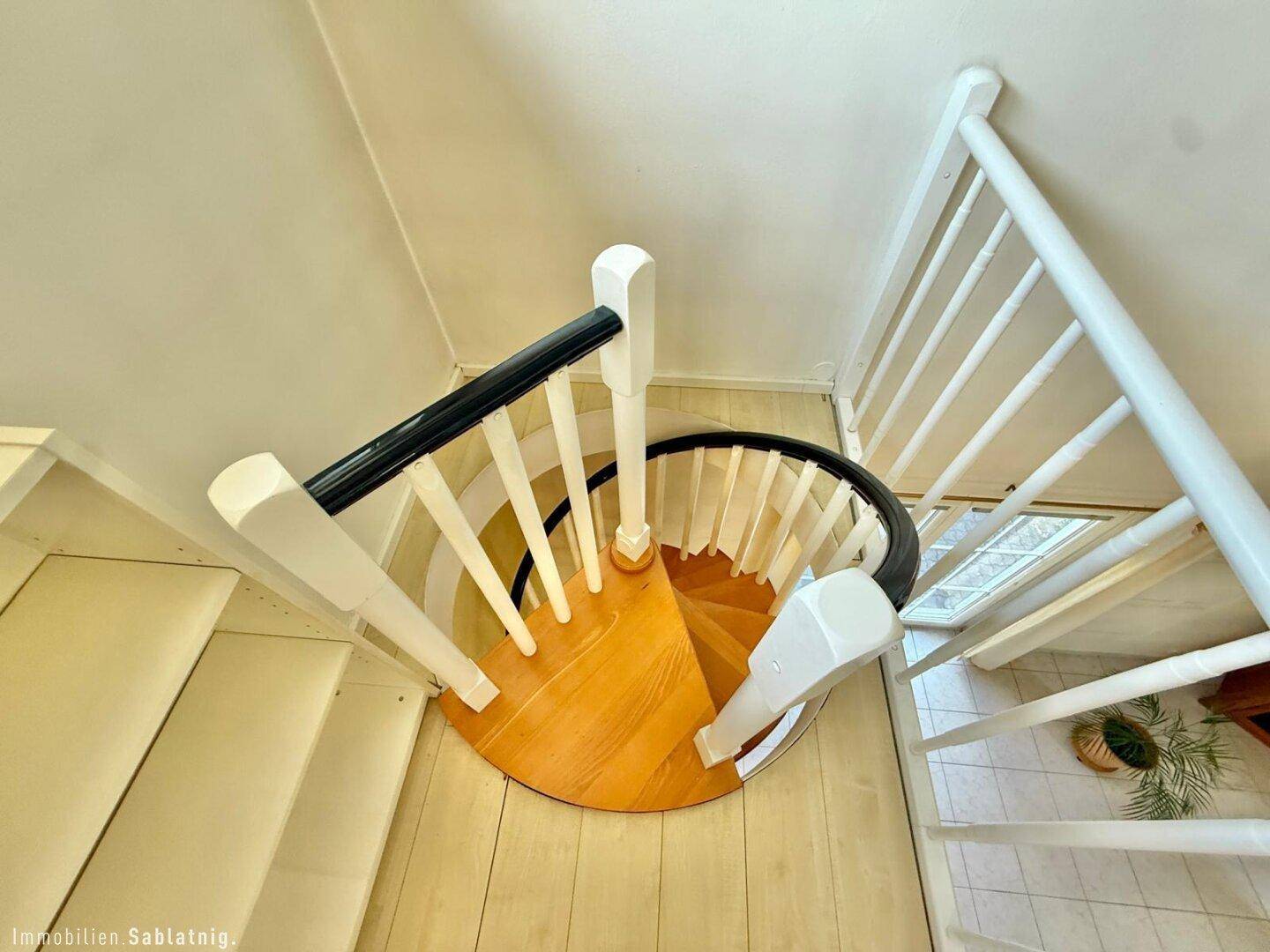 Elegante Wendeltreppe mit Holzstufen und weißem Geländer, die die Etagen verbindet.