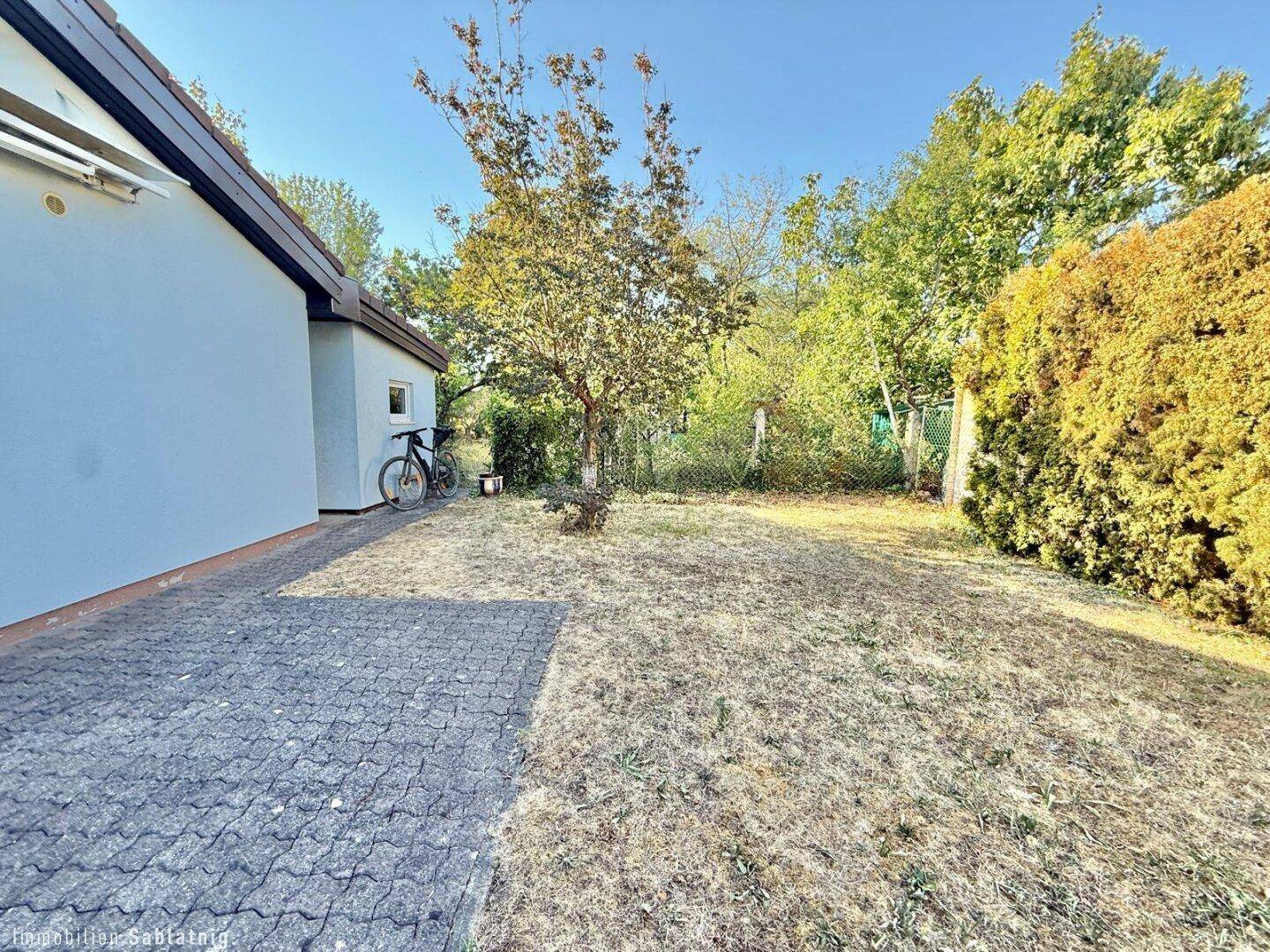 Großer Gartenbereich mit Rasenfläche, Bäumen und gepflastertem Weg.