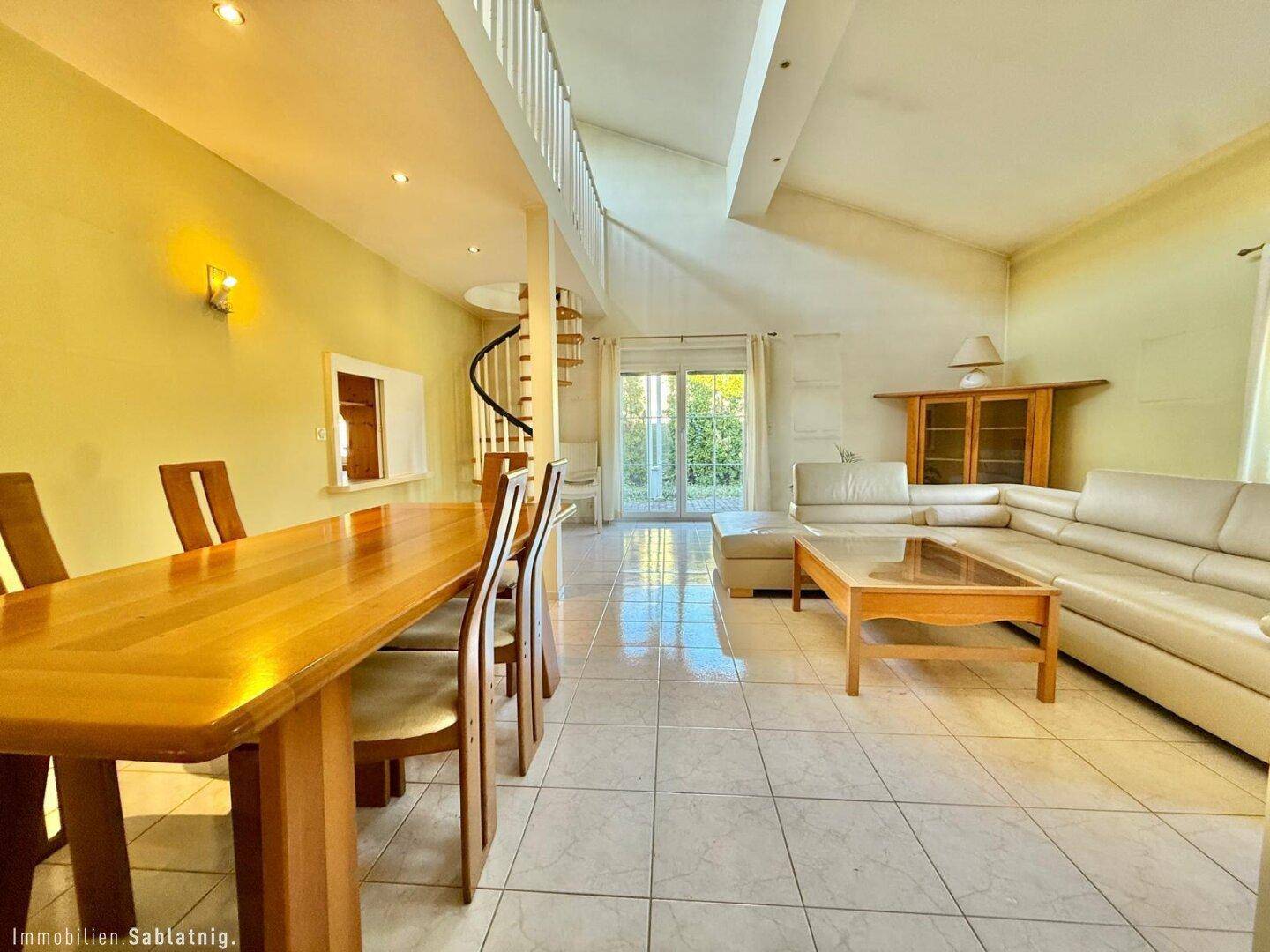 Geräumiger Wohn- und Essbereich mit hohen Decken, Wendeltreppe und Zugang zum Garten.
