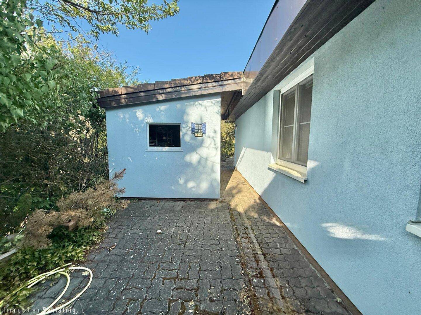 Seitenansicht des Hauses mit gepflastertem Bereich und Zugang zum Garten.