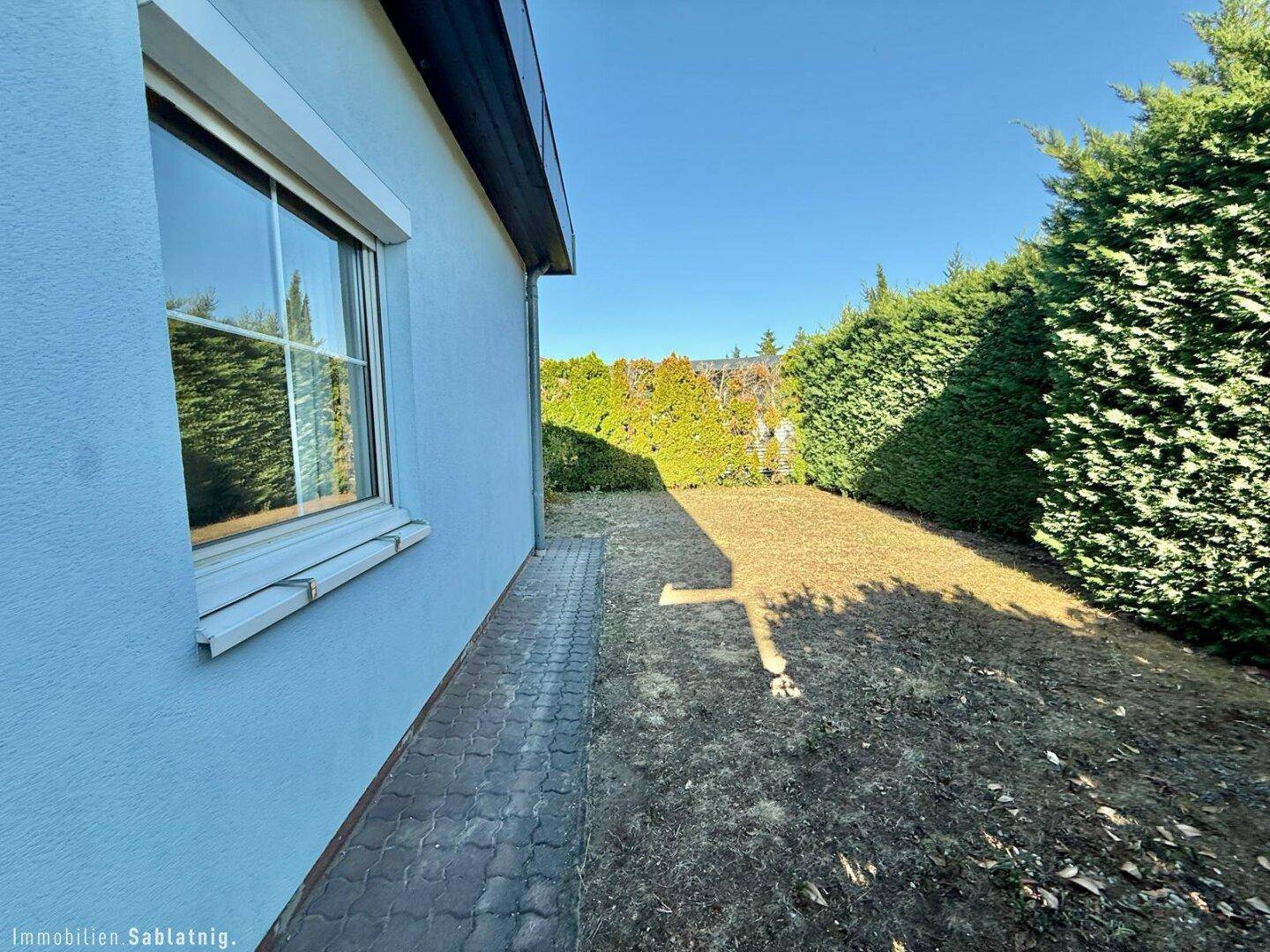 Seitenansicht des Hauses mit schmalem Gartenstreifen und hohen Hecken.