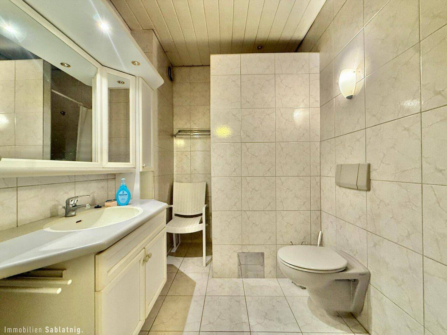 Badezimmer mit Fliesenboden, Einzelwaschbecken, Spiegelschrank und Toilette.