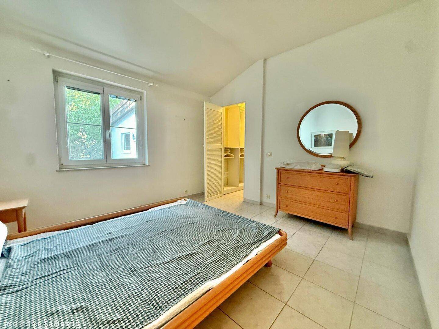 Schlafzimmer mit Fliesenboden, Fenster und Zugang zu einem begehbaren Kleiderschrank.