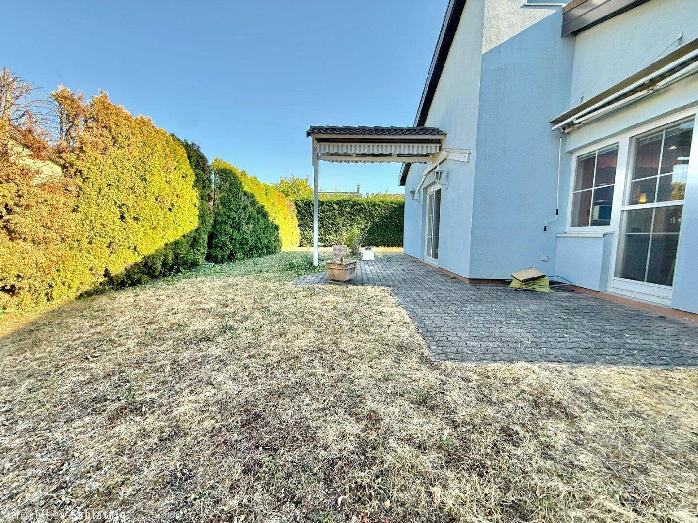 Gartenbereich mit Rasenfläche und gepflasterter Terrasse neben dem Haus.