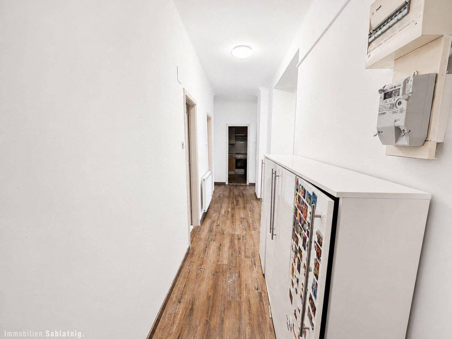 Langer Flur mit Holzoptikboden und sichtbaren Stromzählern an der Wand.