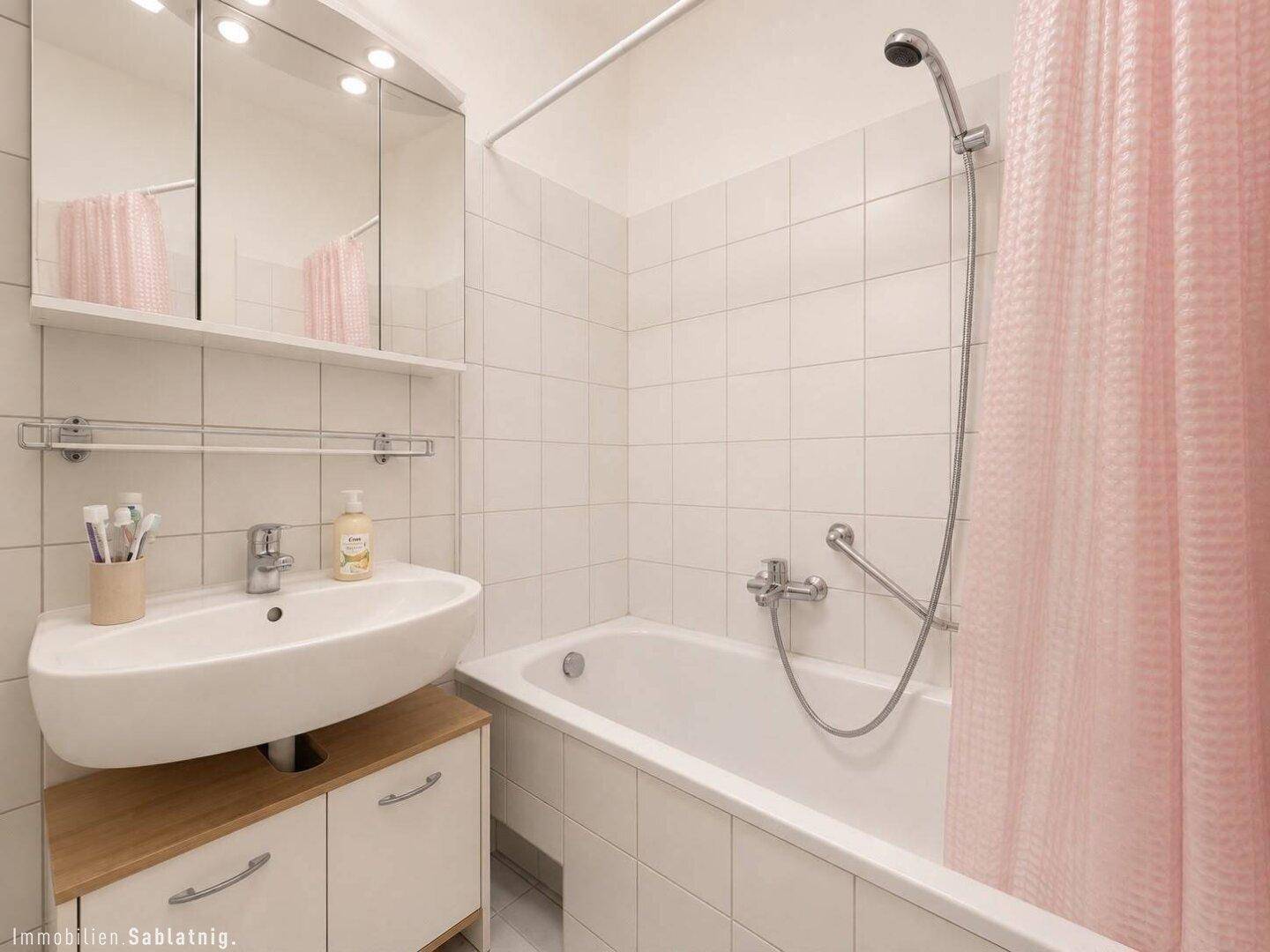 Badezimmer mit weiß gefliesten Wänden, Badewanne und modernem Waschbecken mit Unterschrank.