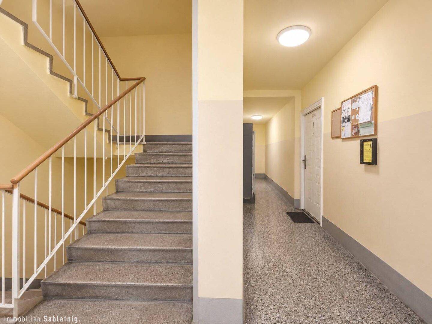 Treppenhaus und Flur im Gemeinschaftsbereich mit Terrazzoboden und gelben Wänden.