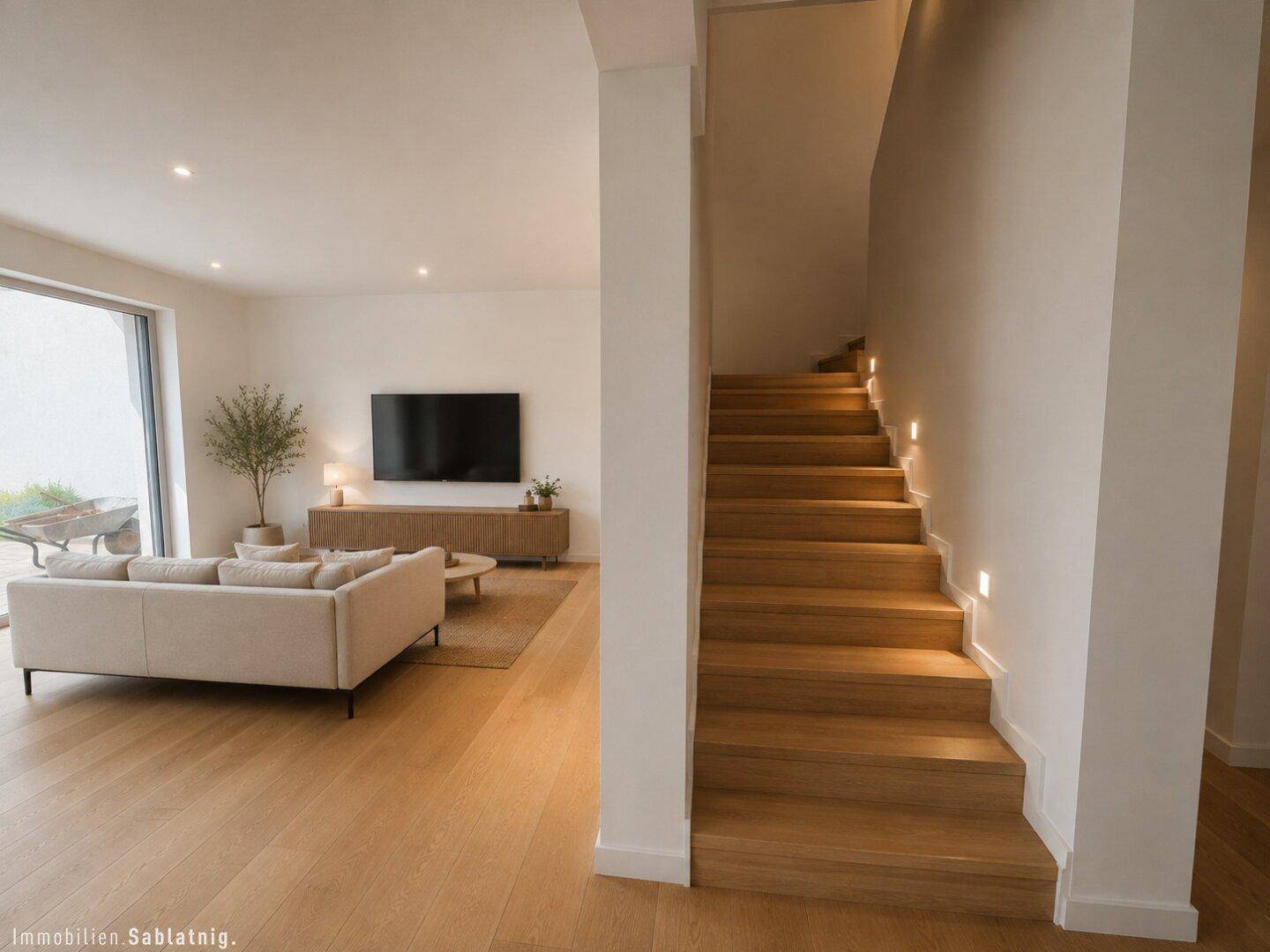 Gemütliches Wohnzimmer mit Sofa, Fernseher und Zugang zu einer modernen Holztreppe.