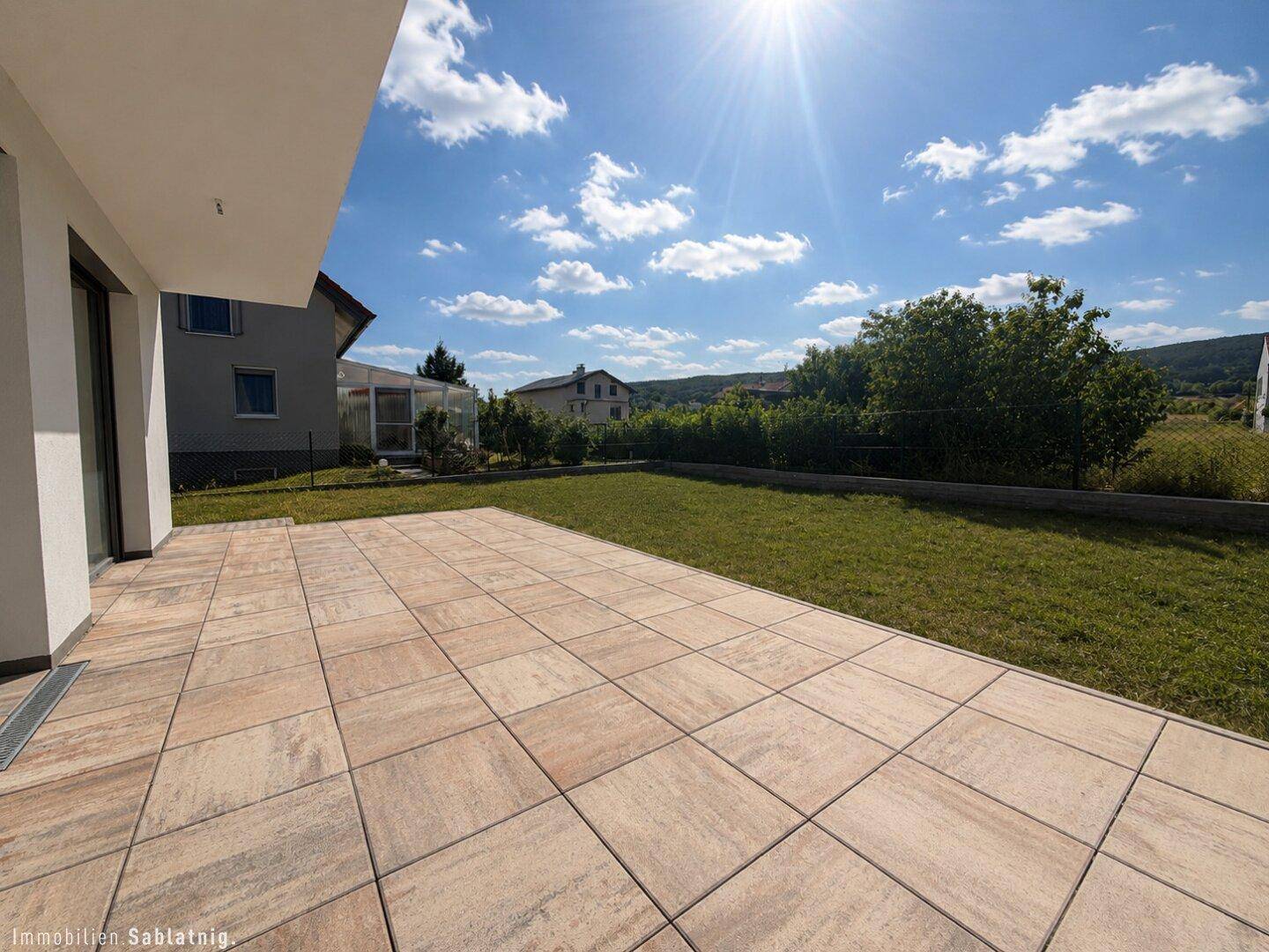 Weitläufige, geflieste Terrasse mit viel Sonnenlicht und Blick auf den Garten.