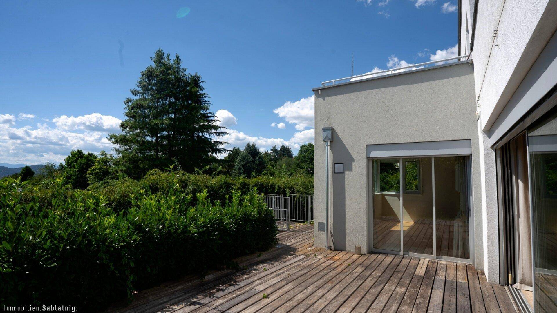 Geräumige Holzterrasse am Haus mit Blick ins Grüne und viel natürlichem Licht.