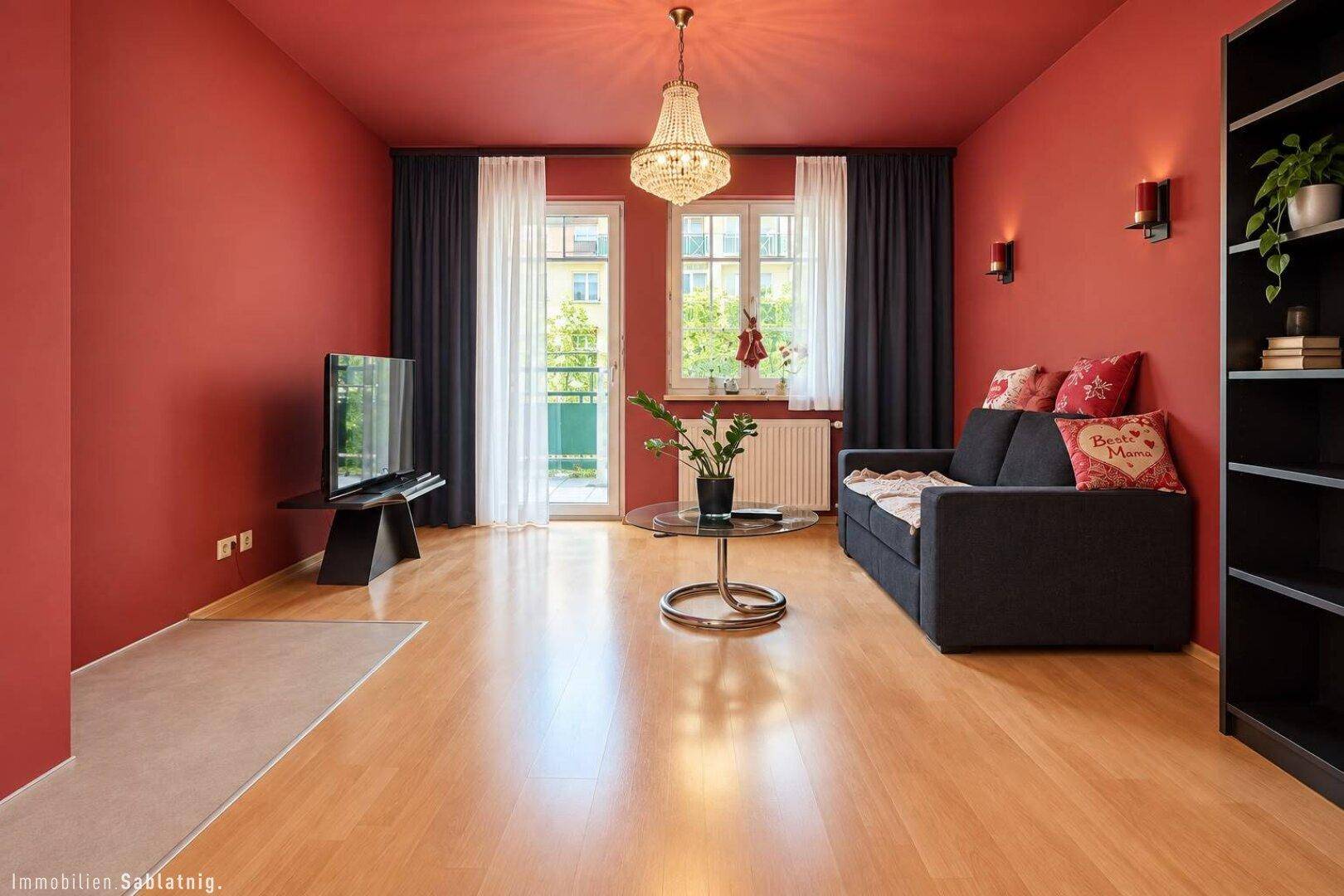 Gemütliches Wohnzimmer mit roter Wandfarbe, Holzboden und Zugang zum Balkon.