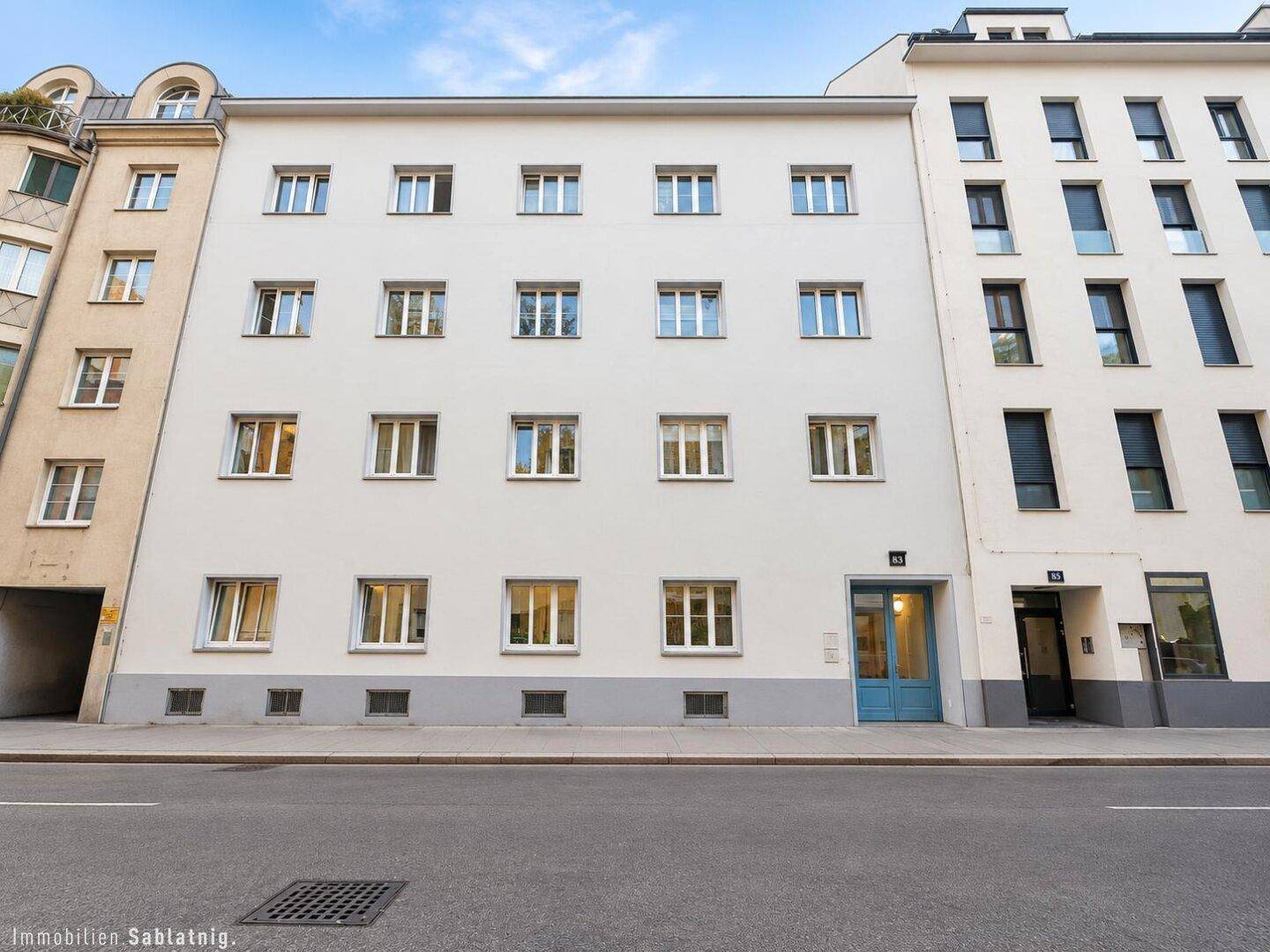 Klassische Fassade eines Mehrfamilienhauses mit vielen Fenstern und einem blauen Eingang.