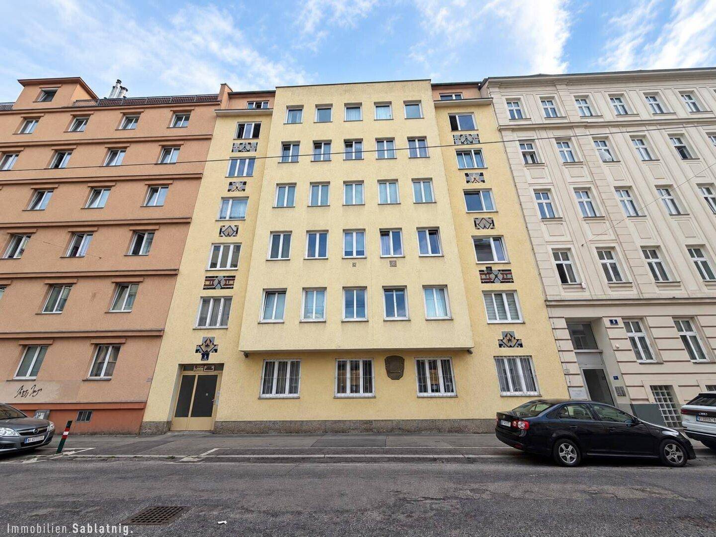 Gelbe Gebäudefassade an einer Stadtstraße mit vielen Fenstern und Autos.