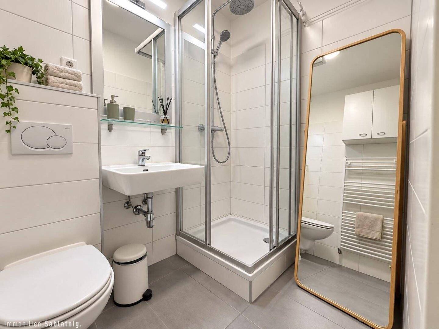 Modernes Badezimmer mit Duschkabine, WC, Waschbecken und großem Spiegel.