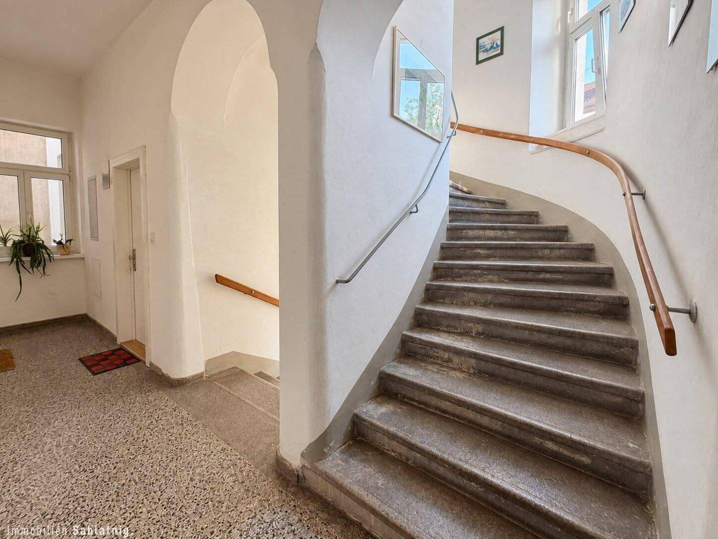 Geschwungenes Treppenhaus mit Steinstufen, Holzgeländer und Fenstern für Tageslicht.