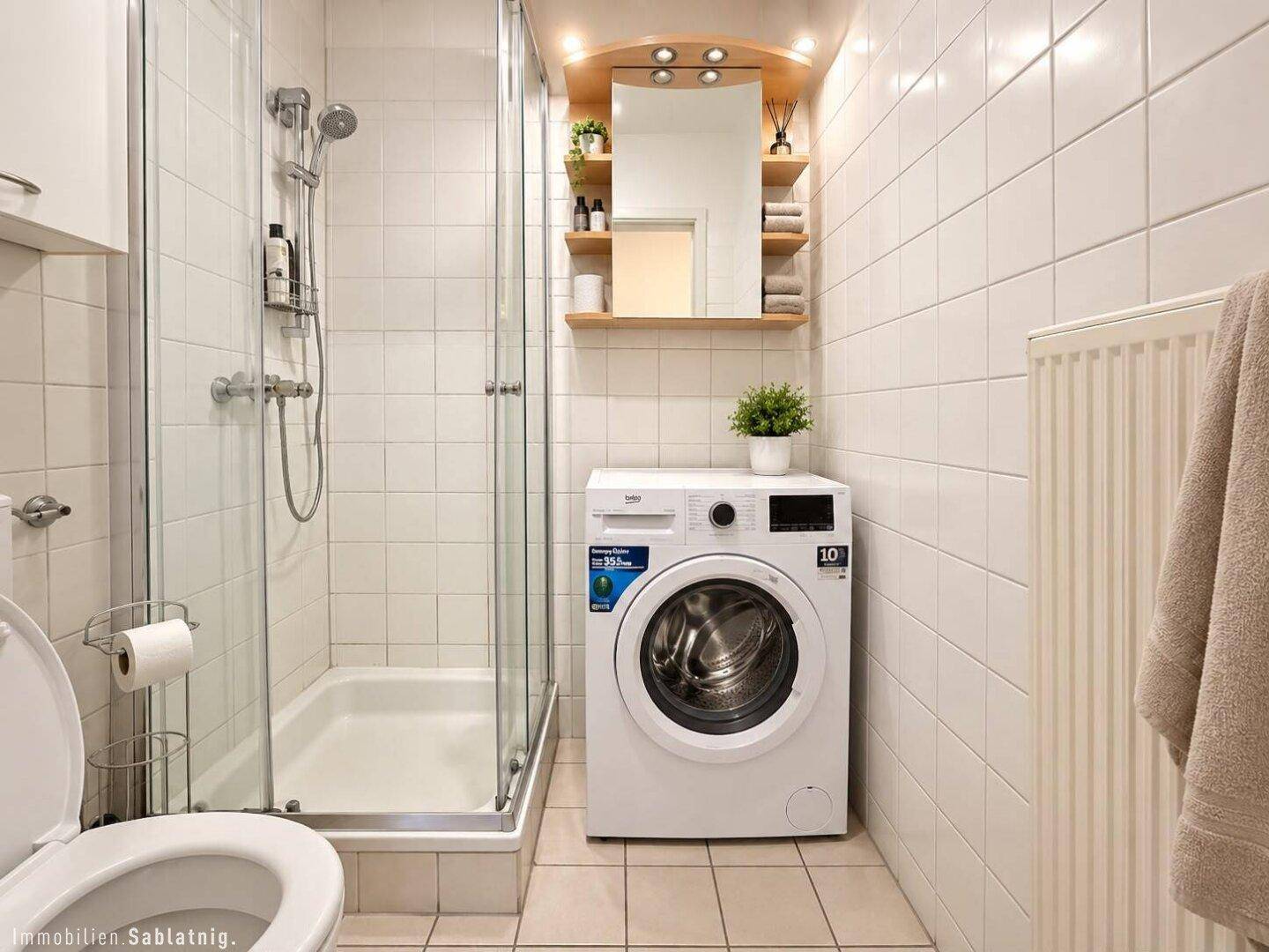 Funktionales Badezimmer mit Duschkabine, Waschmaschine und weißen Fliesen, gut gepflegt.
