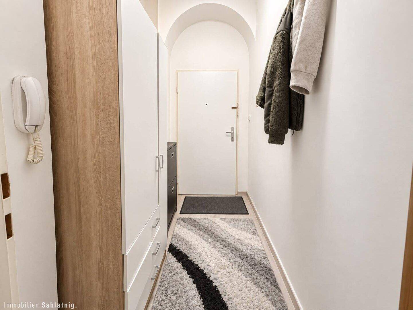 Schmaler Flur mit Garderobe, Schrank und Eingangstür, funktional und hell gestaltet.